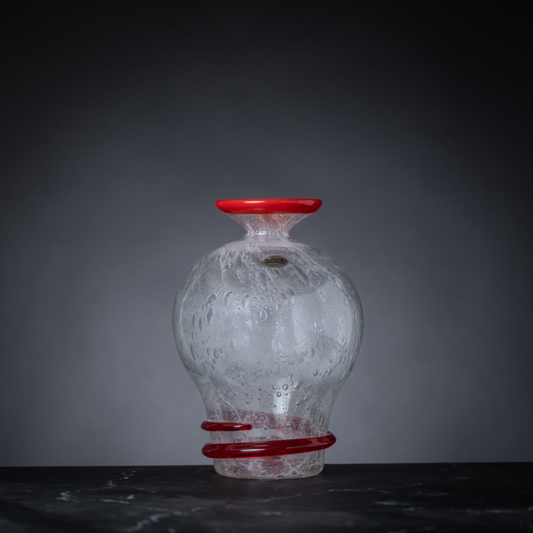 Glass vase with red accents on a dark surface and gray background