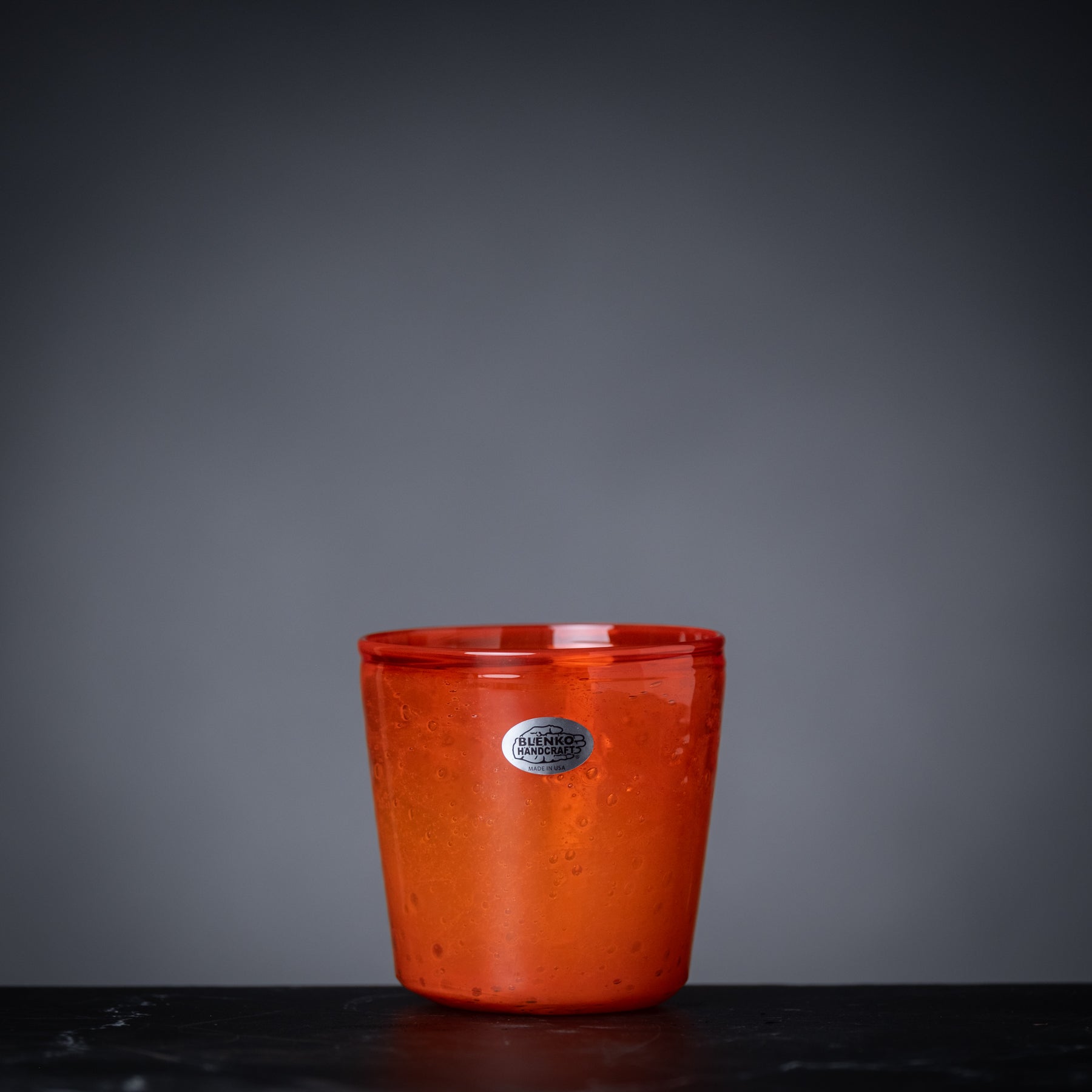 Red glass cup with a silver label on a dark surface and gray background