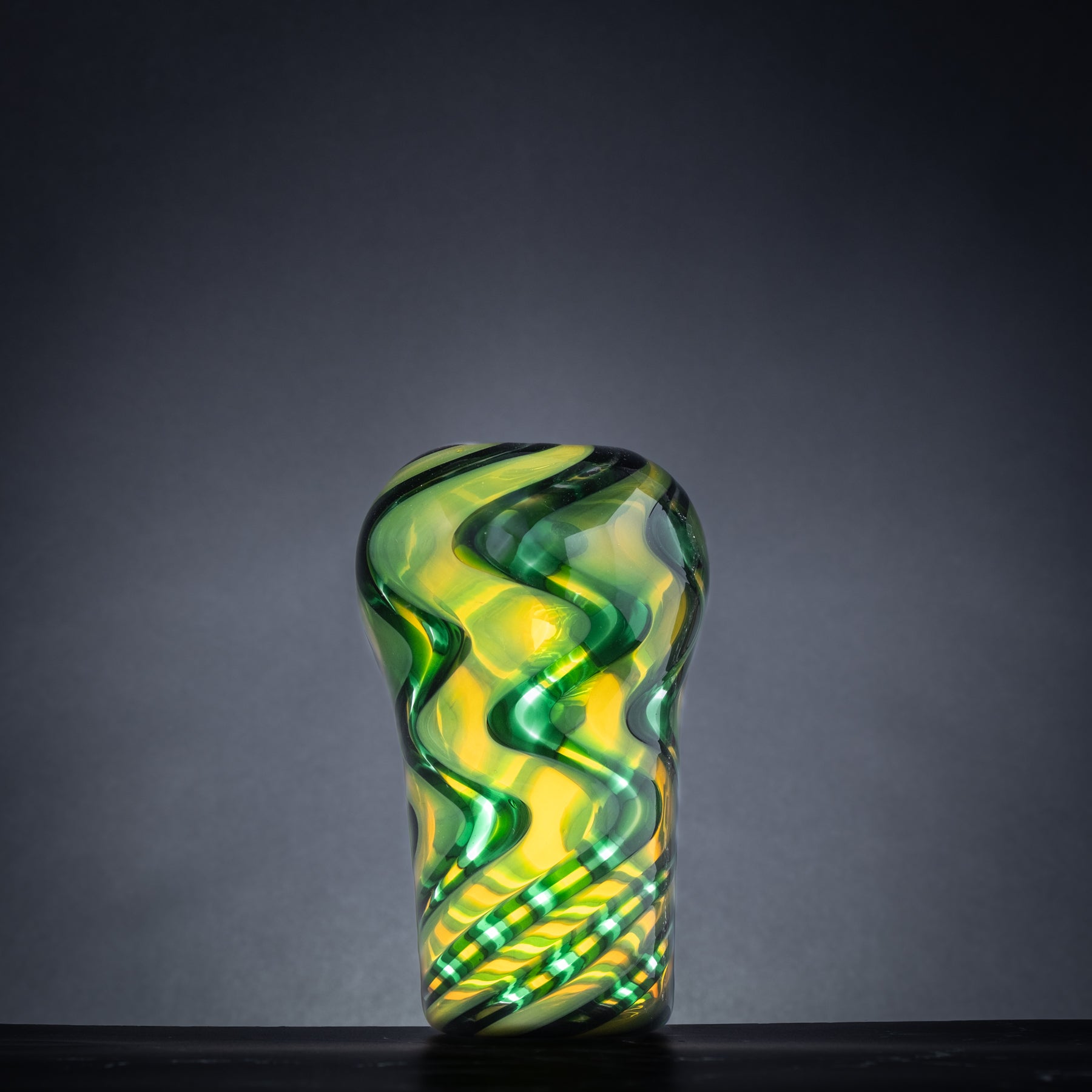 Glass vase with green and yellow wavy pattern on a dark background