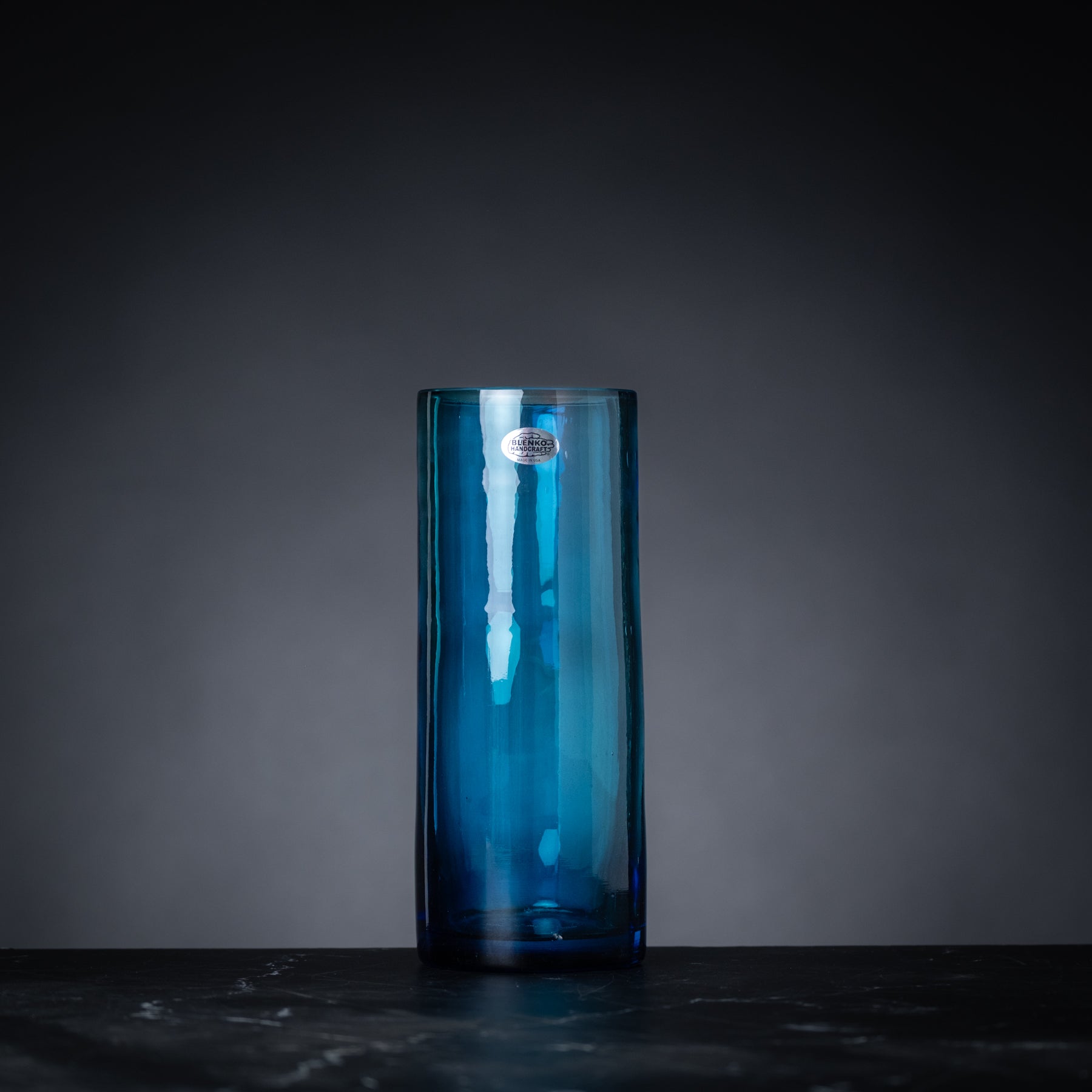 Blue glass vase on a dark surface with a gray background
