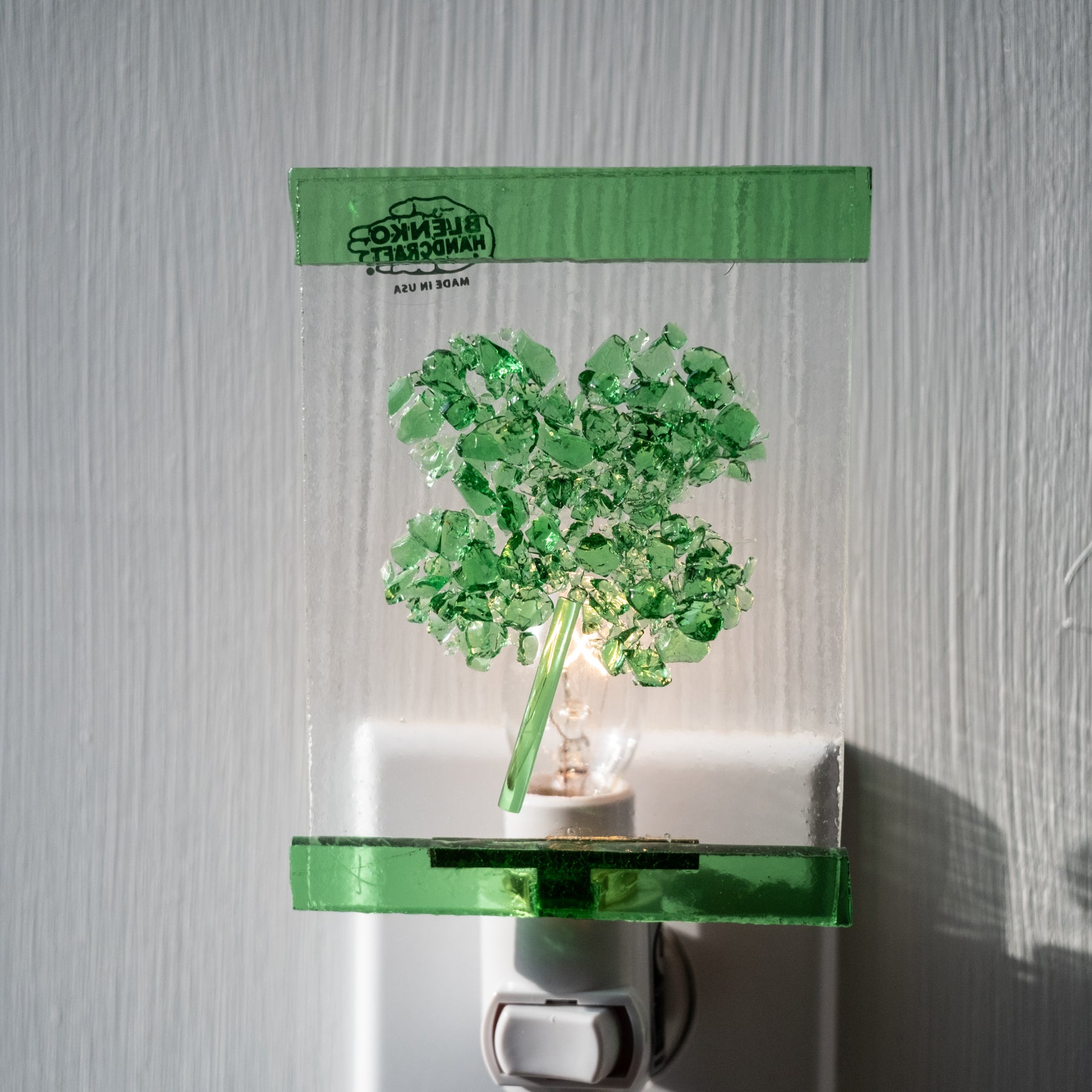 Green glass night light with decorative tree design on a white wall.