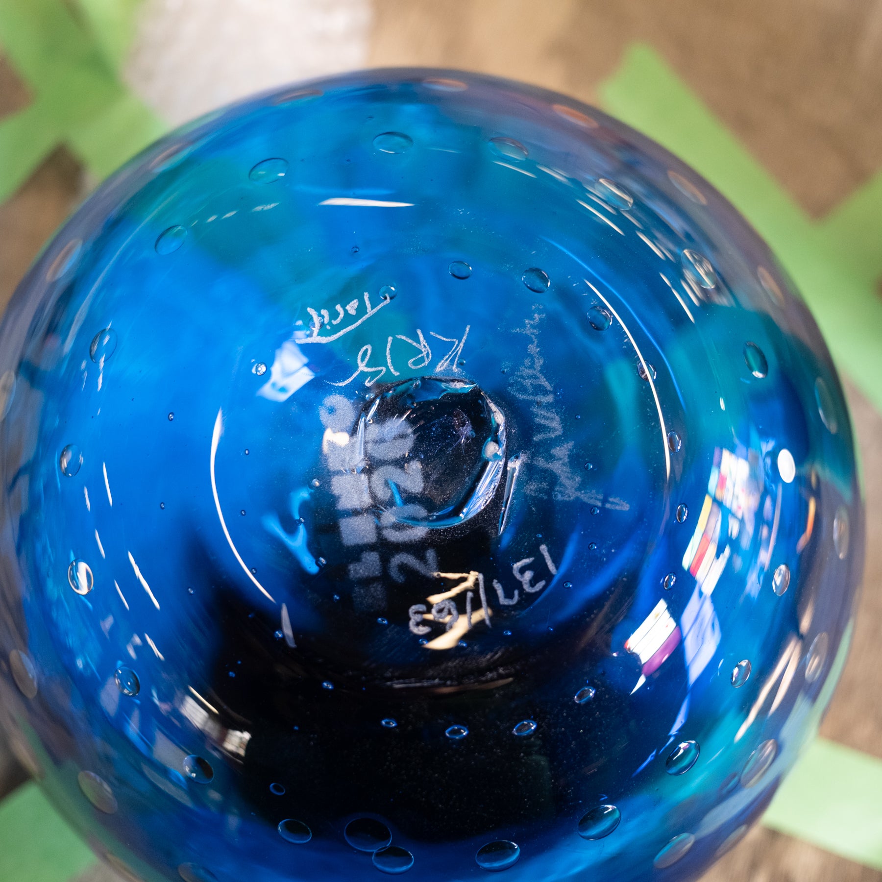 A close-up of a blue glass bowl with a textured bubble pattern and hand-written markings on the inside base.