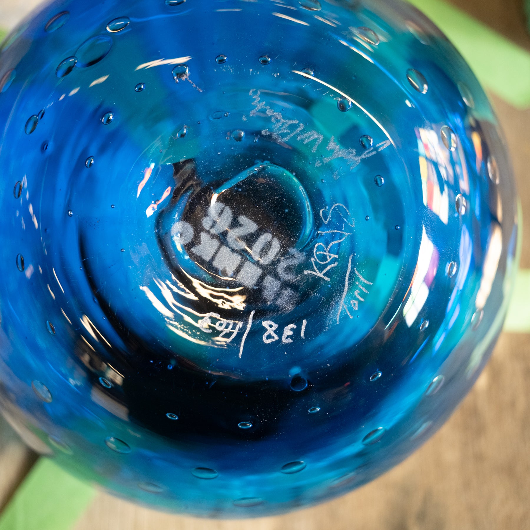 Close-up of the bottom of a blue glass bowl or vase with a textured, bubble-covered surface and white hand-written markings.