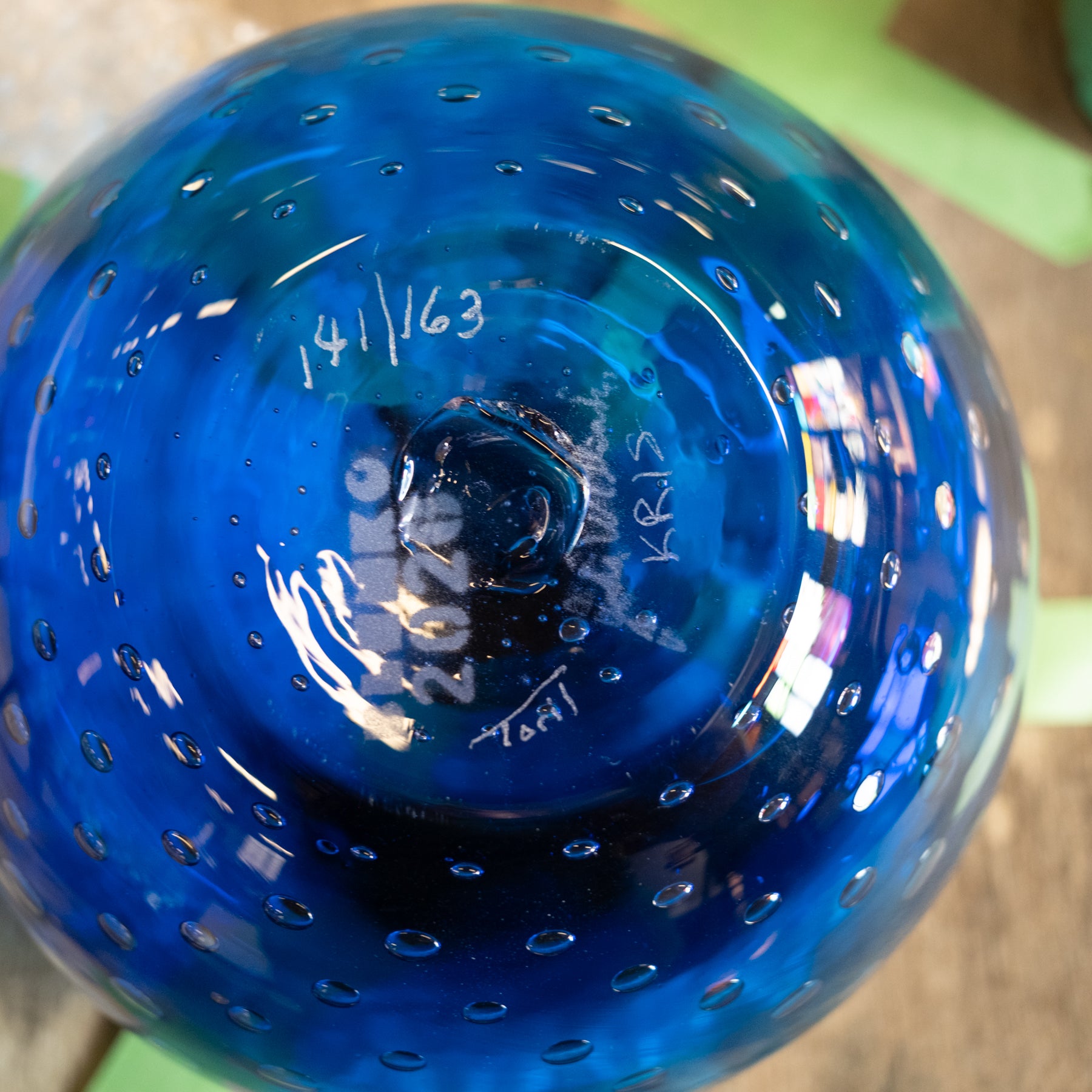 A close-up of a blue glass bowl viewed from above, showing a textured surface with small raised dots and handwritten markings on the inside bottom.