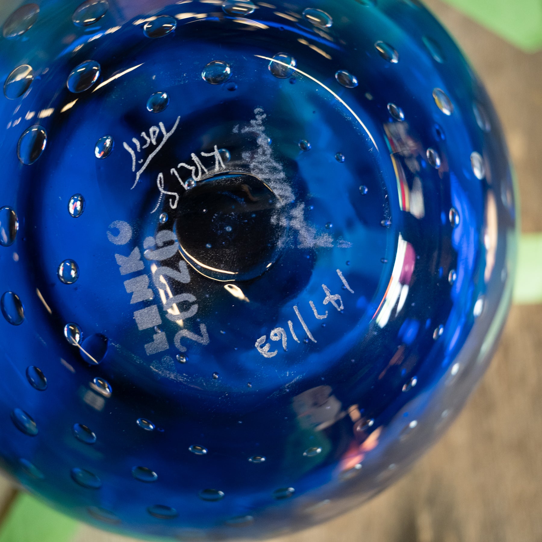 A close-up of the bottom of a cobalt blue glass bowl with a bubble pattern and white printed markings including 'HENKO' and date '02/02/2023'.