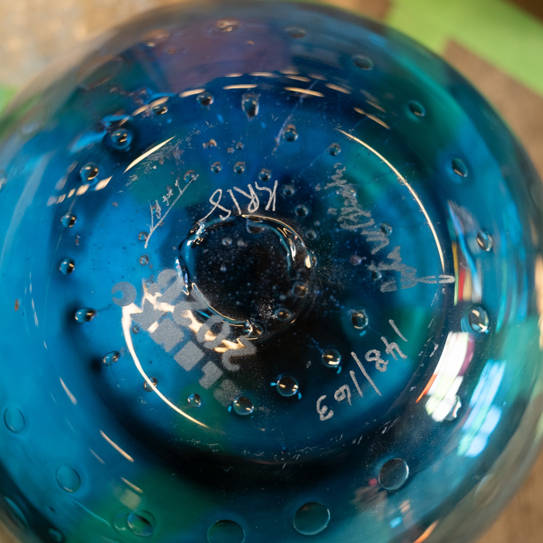 Close-up of the bottom of a transparent blue glass container or bottle with embossed circular text and bubble-like perforations around the rim.
