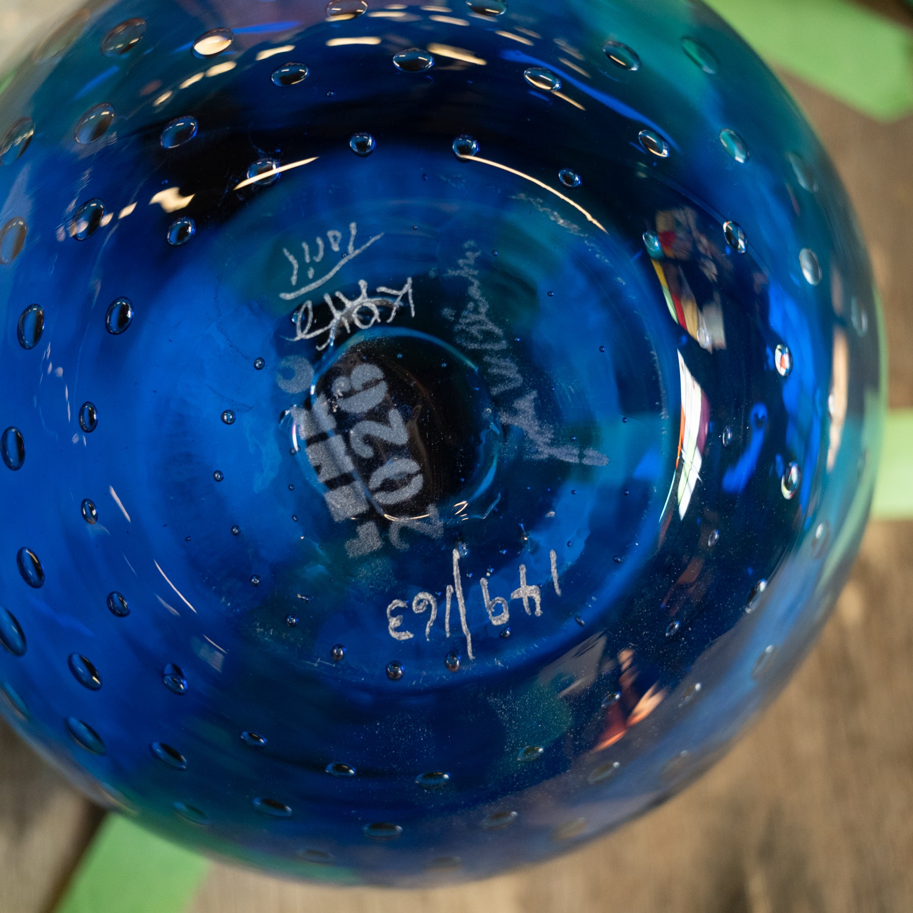 A close-up of the bottom of a vibrant blue glass bowl with a bubble pattern and white hand-written markings.