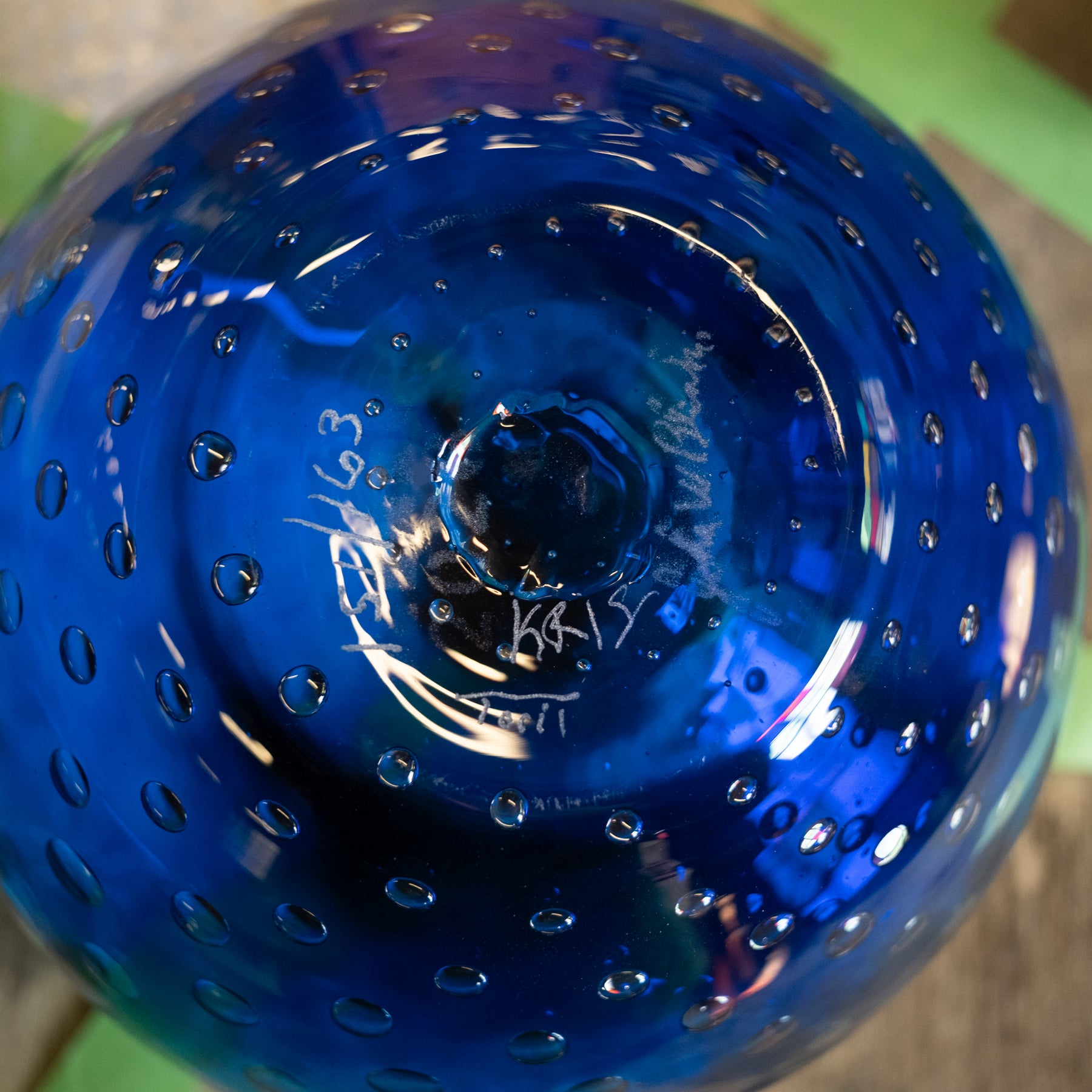 A close-up of a cobalt blue glass bowl with a textured, perforated surface and white hand-written markings on the bottom.