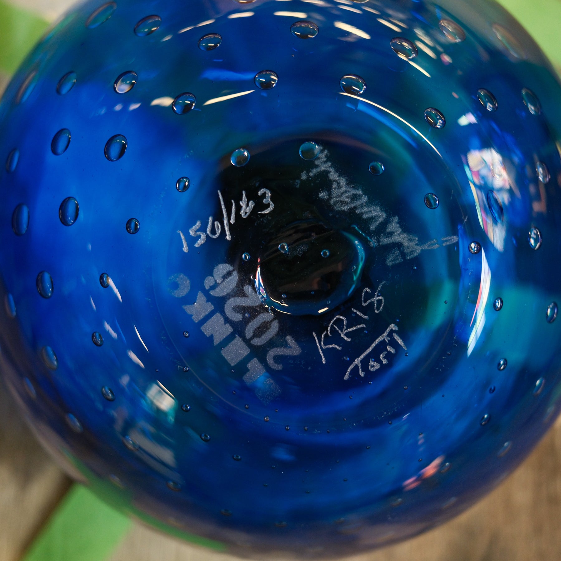 Close-up of a glossy cobalt blue glass bowl with a bubble pattern and white hand-written markings on the inside base.