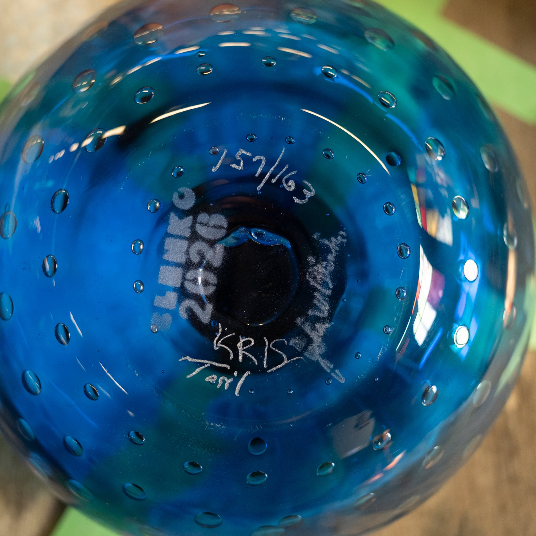 Close-up of a blue glass bowl with a perforated pattern and white handwritten markings on the inside, including the name 'Lemko' and date '7-17-63'.