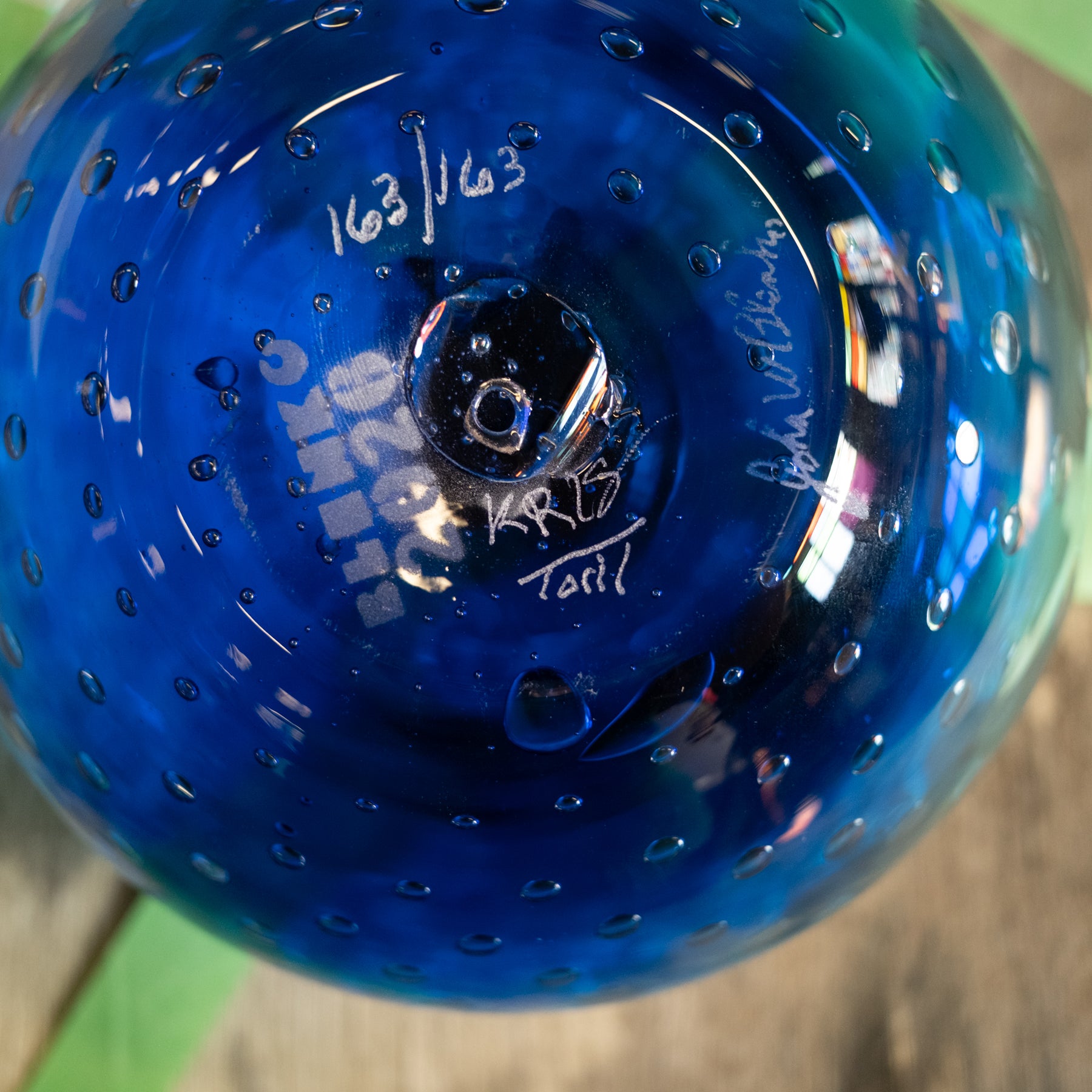 Close-up of a blue glass bowl with a textured, bubble-covered surface and white hand-written markings on the inside base.