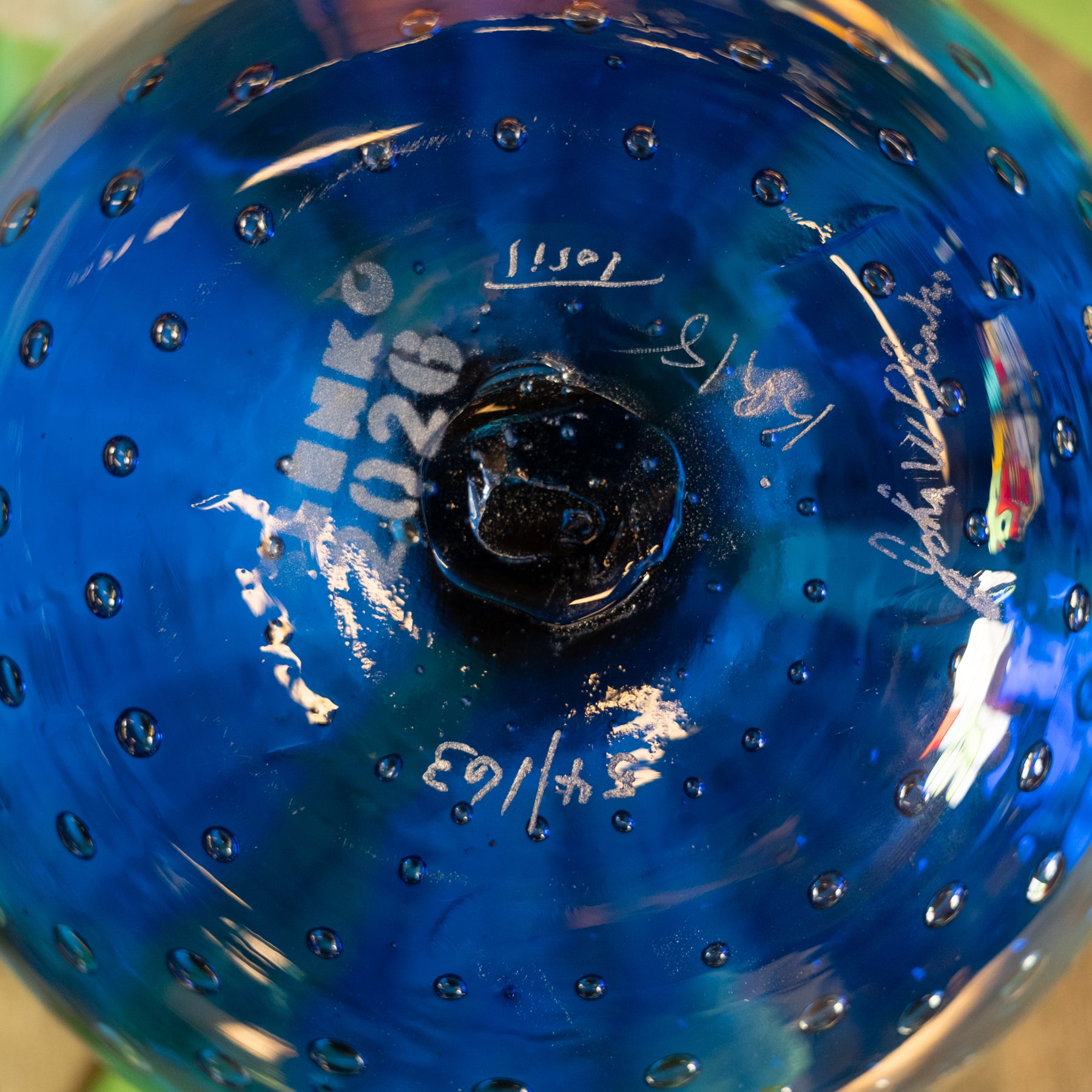Close-up of the bottom of a blue glass bowl with a bubble pattern and white hand-written markings.