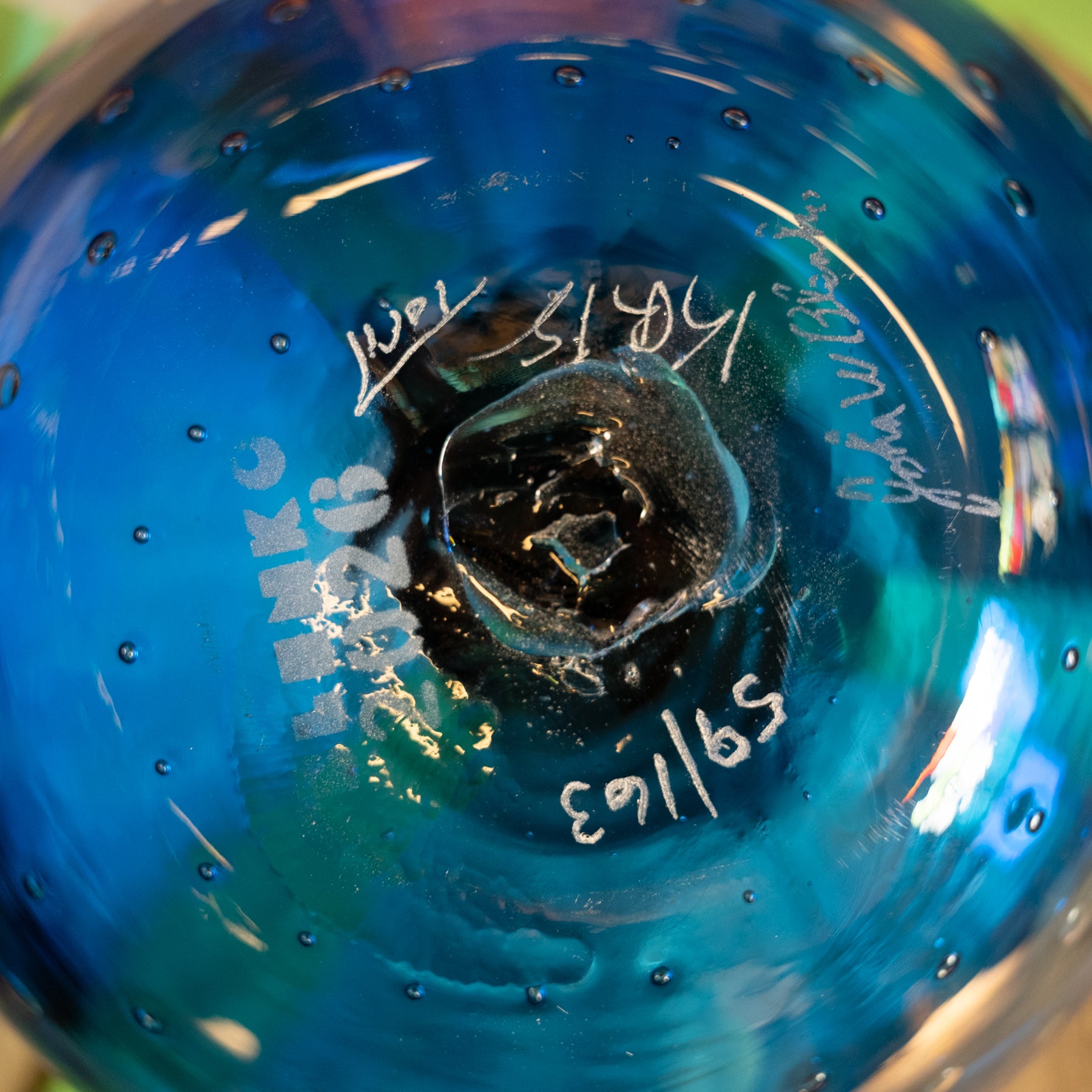 Close-up of the base of a blue glass bowl or vase with hand-written markings and serial numbers on the clear glass.