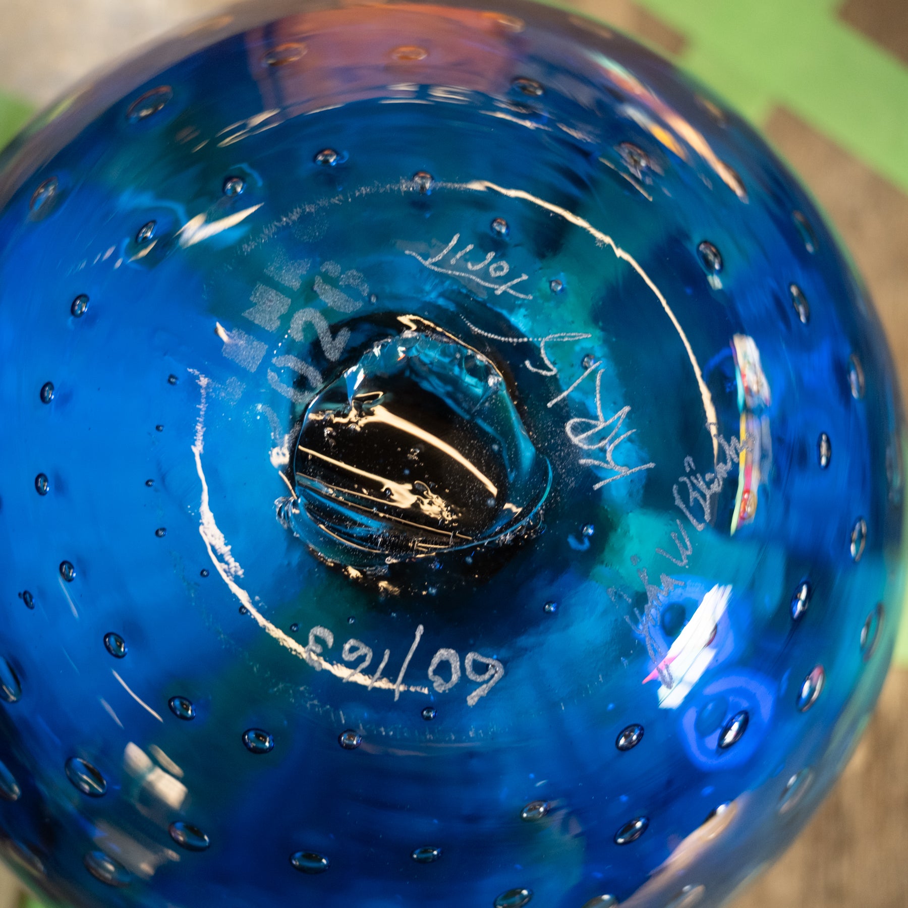 A close-up of a blue glass bowl with a textured bubble pattern and a black center base, showing white hand-written markings on the inside.