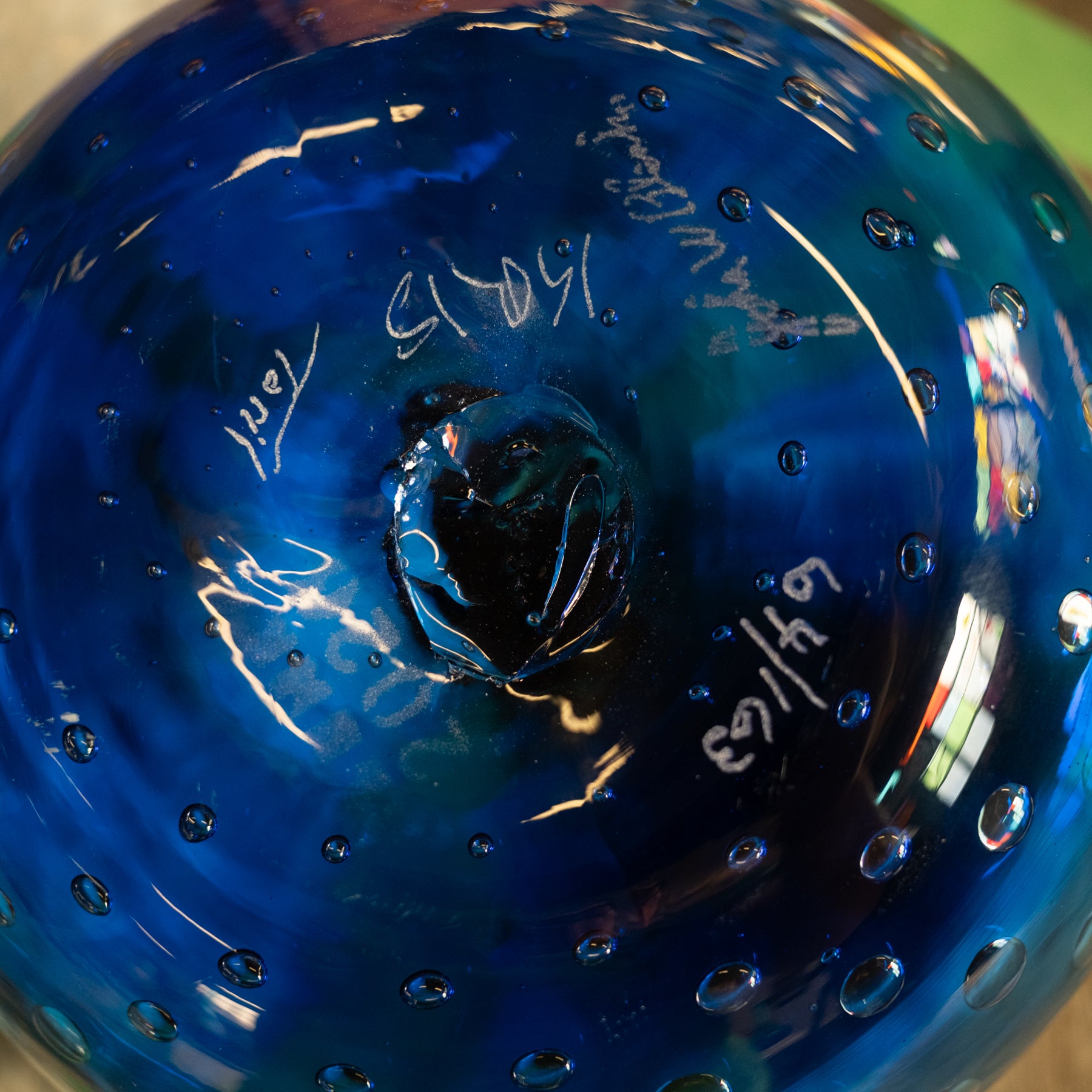 Close-up of the bottom of a cobalt blue glass bowl with bubble texture, handwritten markings, and a reflective finish.