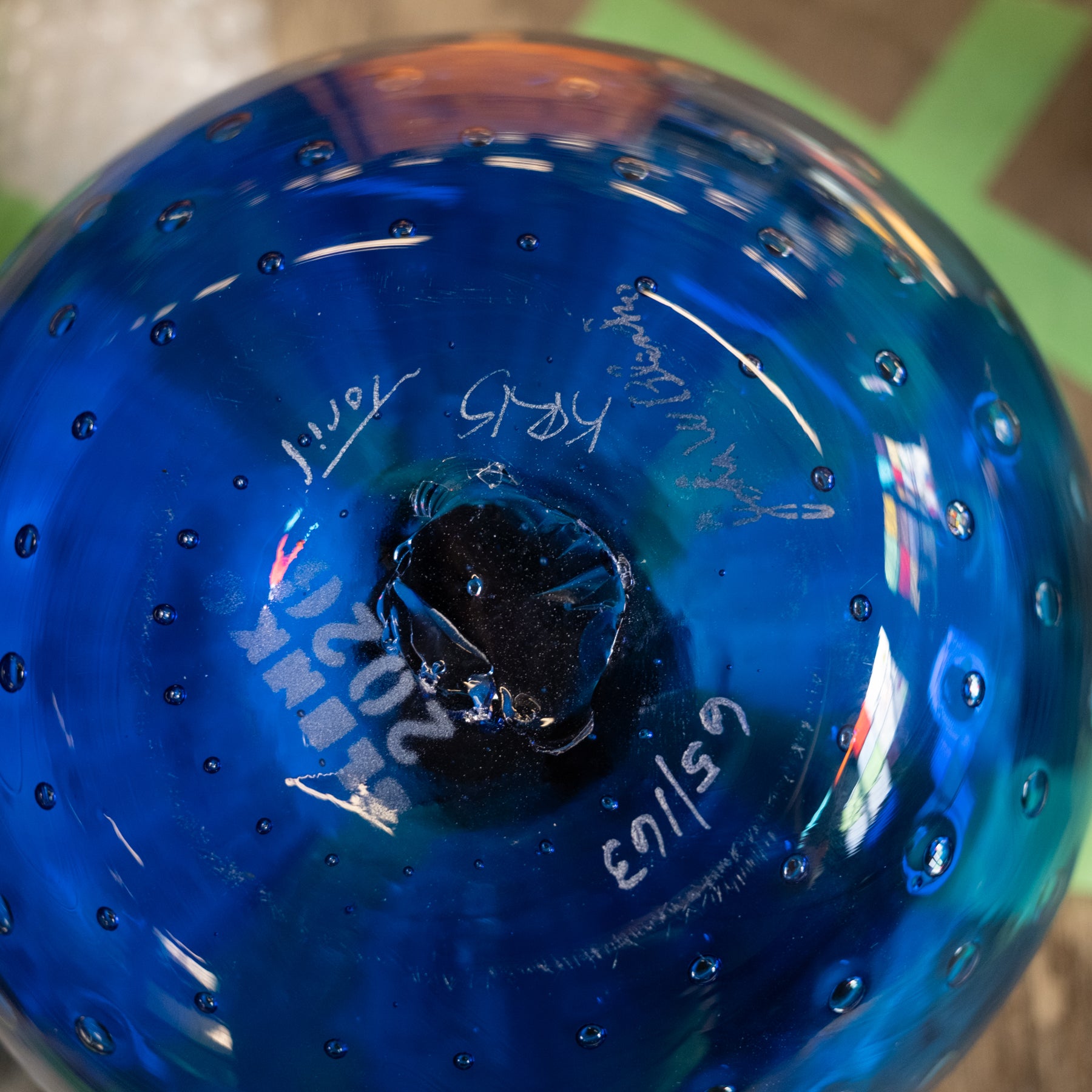 A close-up of a blue glass container or bottle base with a glossy finish, visible hand-written markings, and small bubble details around the rim.