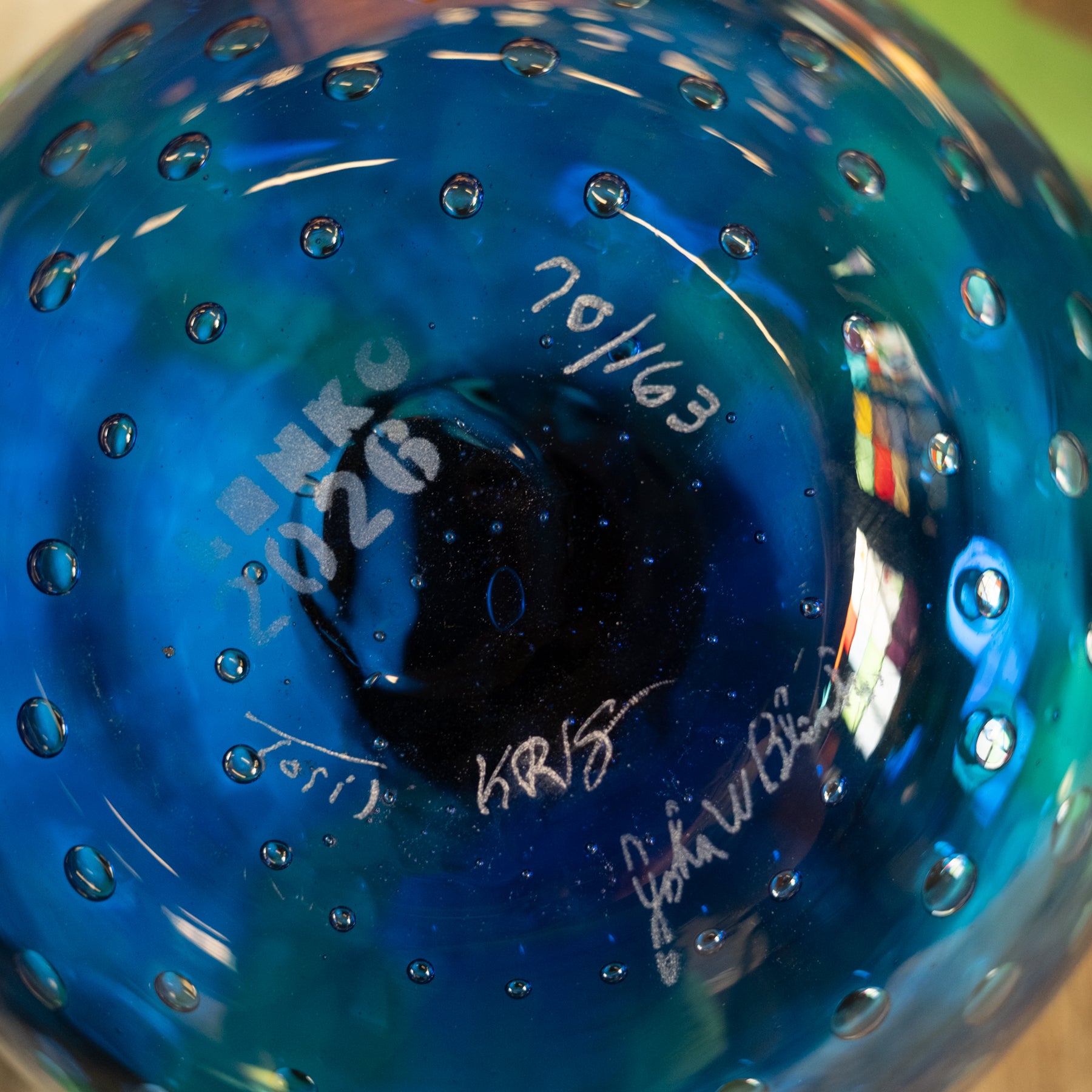 Close-up of the bottom of a blue glass bowl with a bubble pattern, featuring white handwritten markings and signatures.