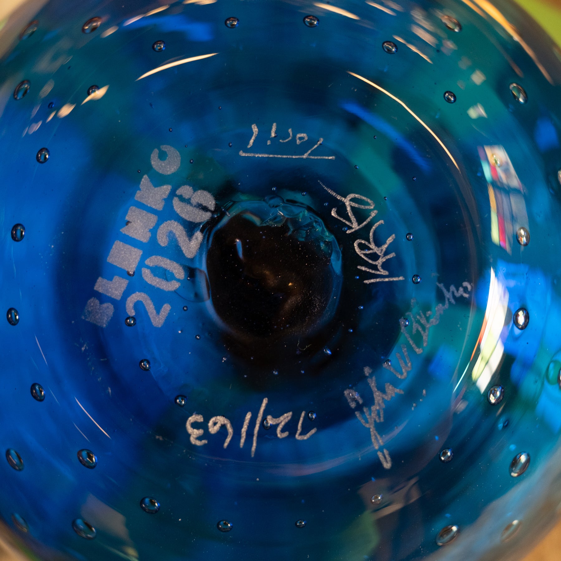 Close-up of a blue glass bowl or vase with white handwritten markings and signatures on the inside surface.