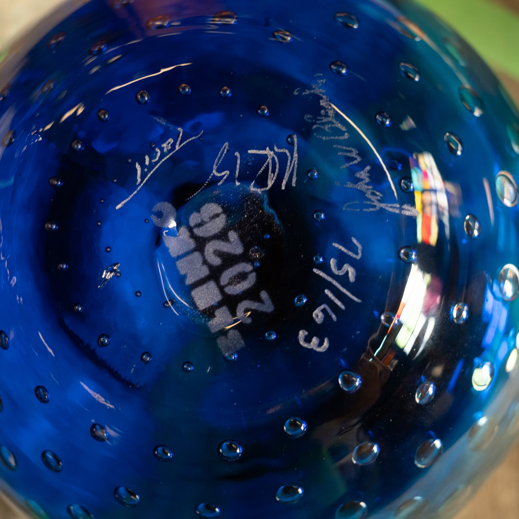Close-up of the inside of a cobalt blue glass bowl or vase with a bubble pattern and white handwritten markings on the bottom.