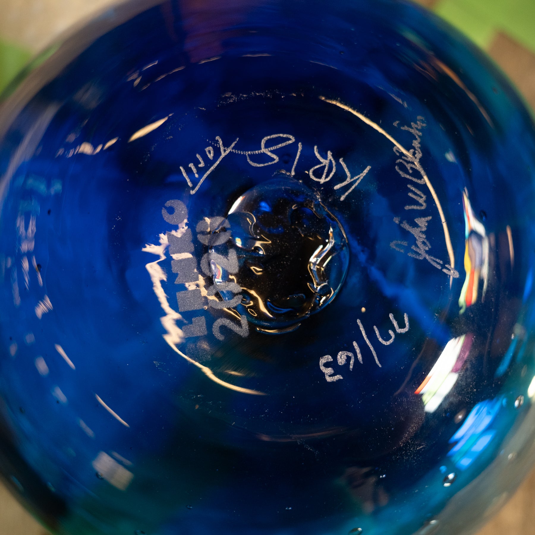 Close-up of the bottom of a blue glass container or bottle with white handwritten markings and reflections.