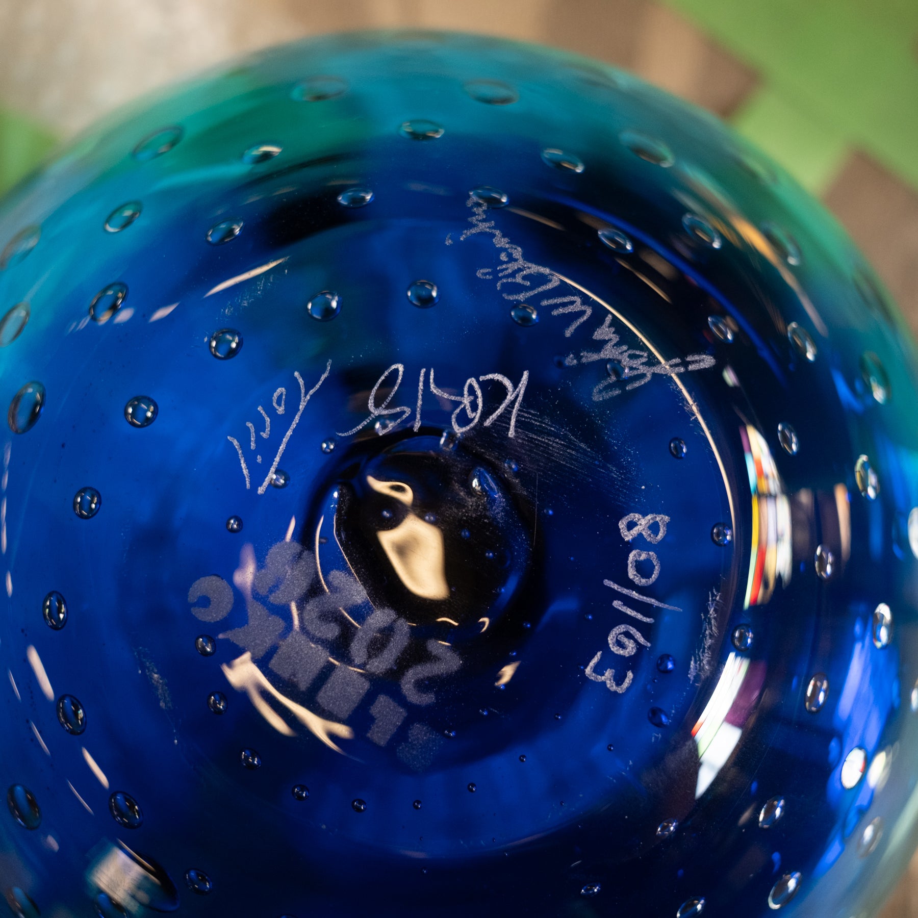 Close-up of the bottom of a cobalt blue glass vessel with a textured bubble pattern and white handwritten markings.