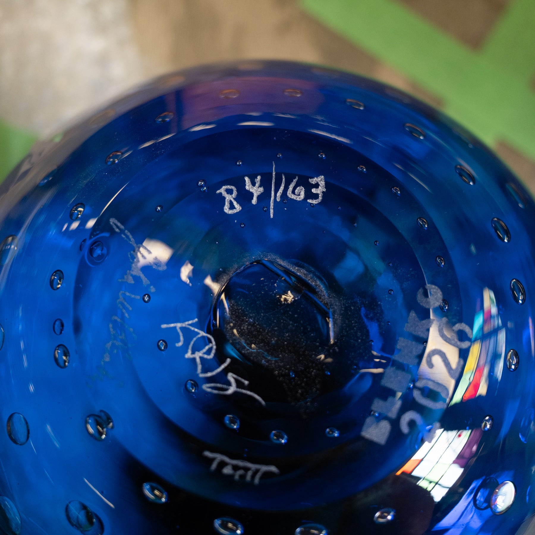 Close-up of a blue glass object with embossed circular perforations and white handwritten markings, photographed tightly against a blurred background.