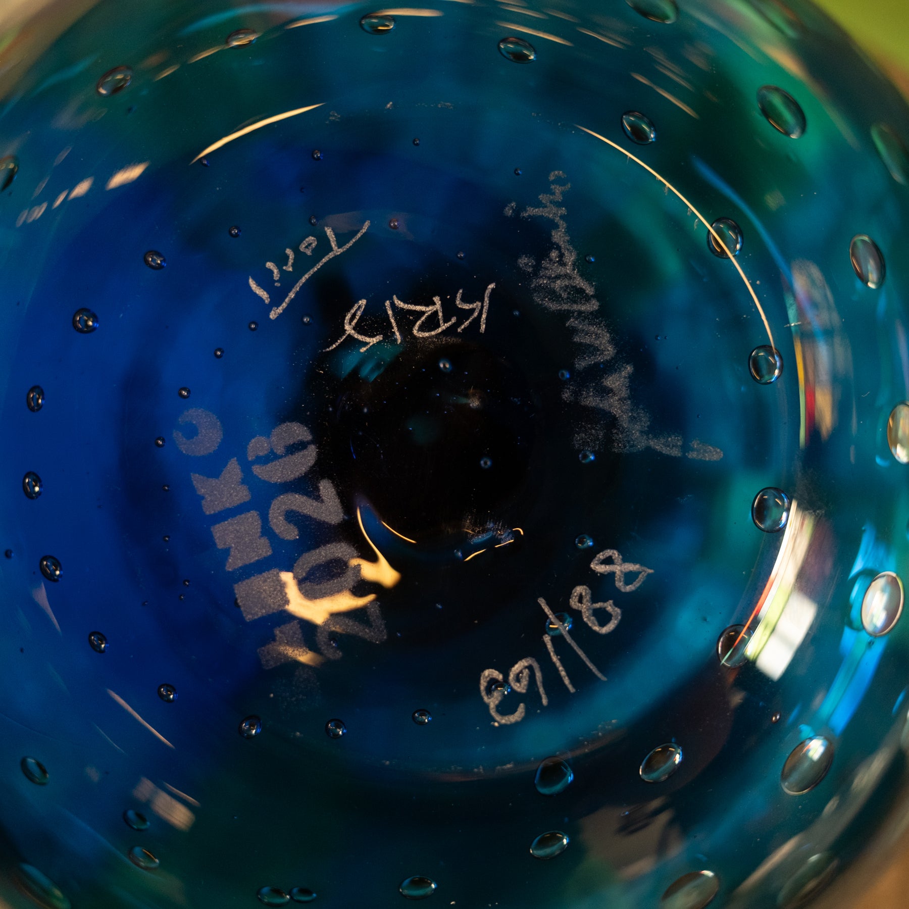 Close-up of the inside of a blue glass bowl or vase with embossed white text and handwritten markings, including 'C. H.