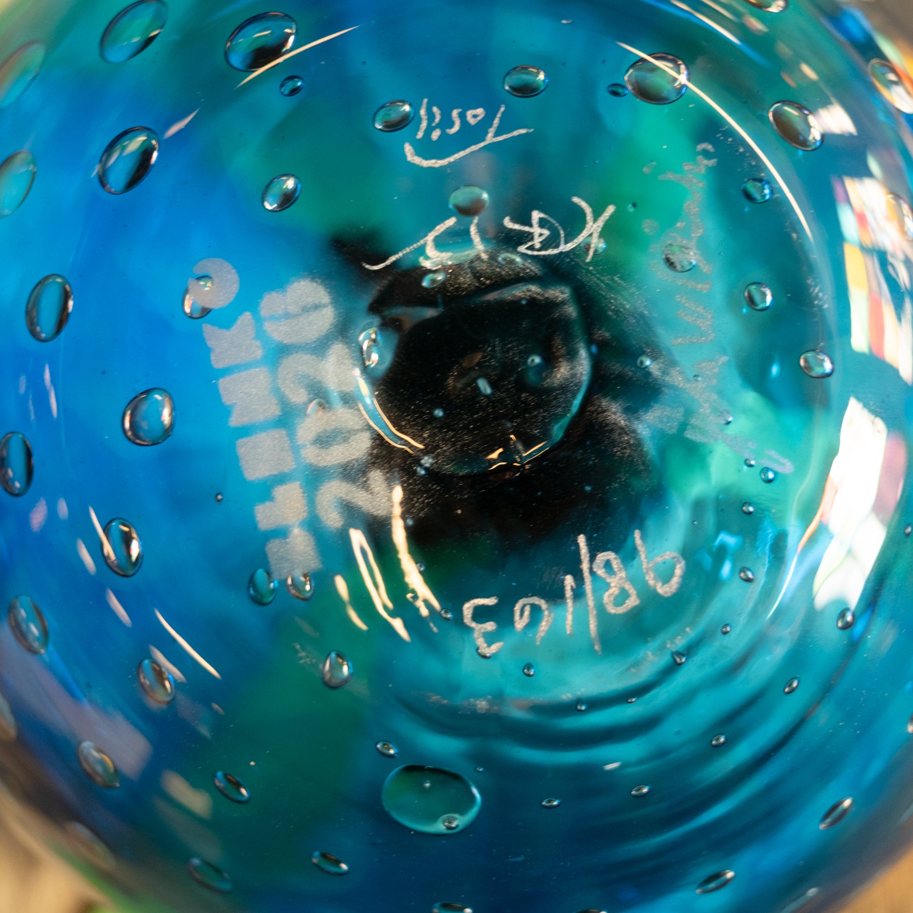 Close-up of a blue glass container or bottle with water droplets on the surface, showing white handwritten markings and a dark central area.