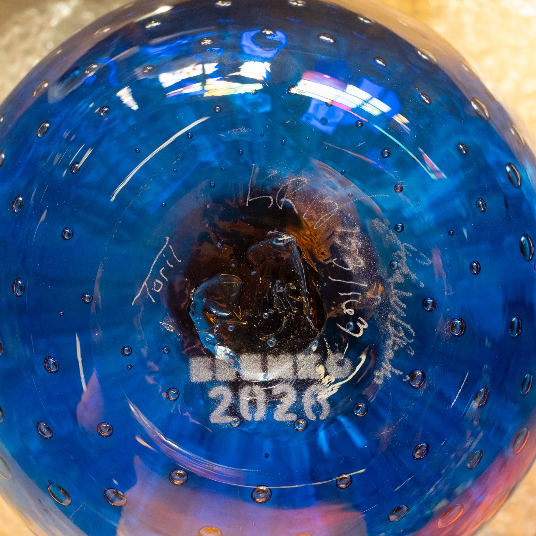 A close-up of a blue glass bowl with a textured bubble pattern and white printed text reading 'BONSAI 2026' near the bottom center.