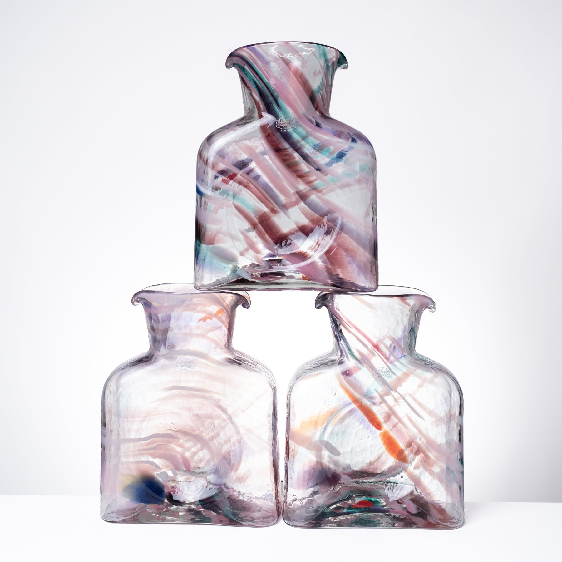 Three hand-blown glass bottles with a stacked arrangement, featuring translucent clear glass with colorful swirls of pink, purple, blue, and orange.