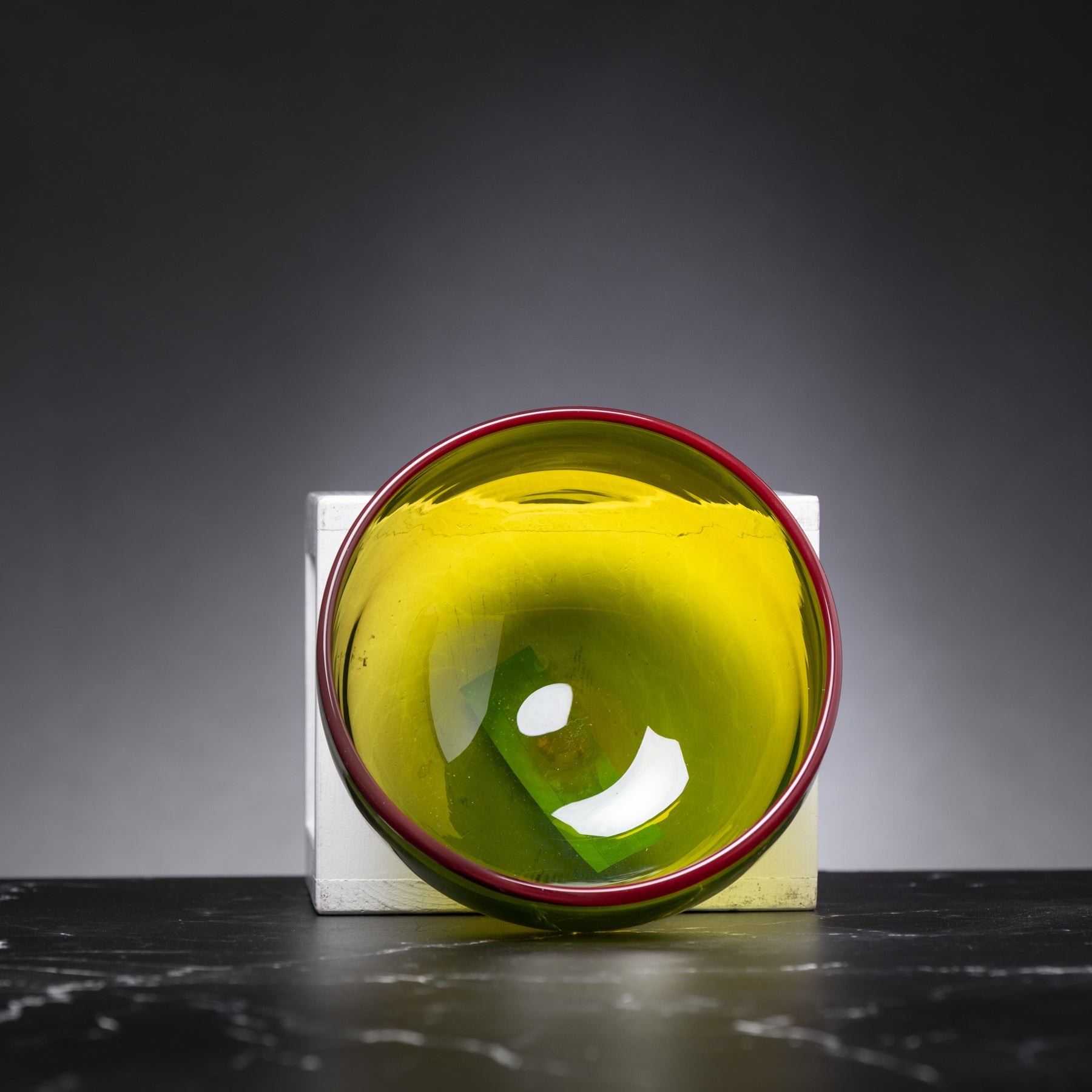 Green glass bowl with red rim on a black surface against a gray background