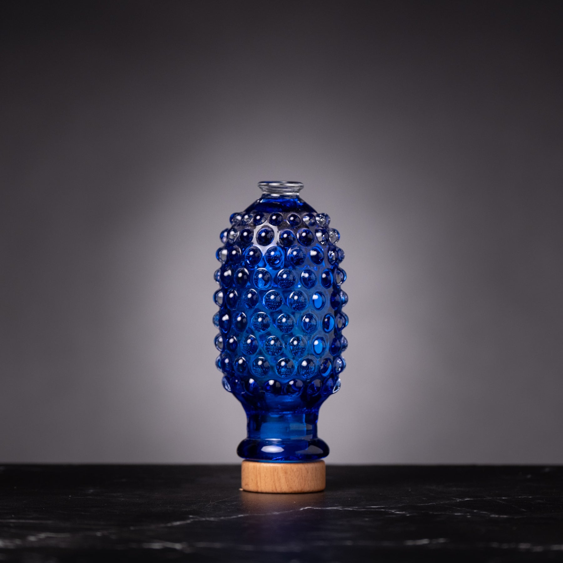 Blue textured glass bottle with wooden base on a dark surface and gray background