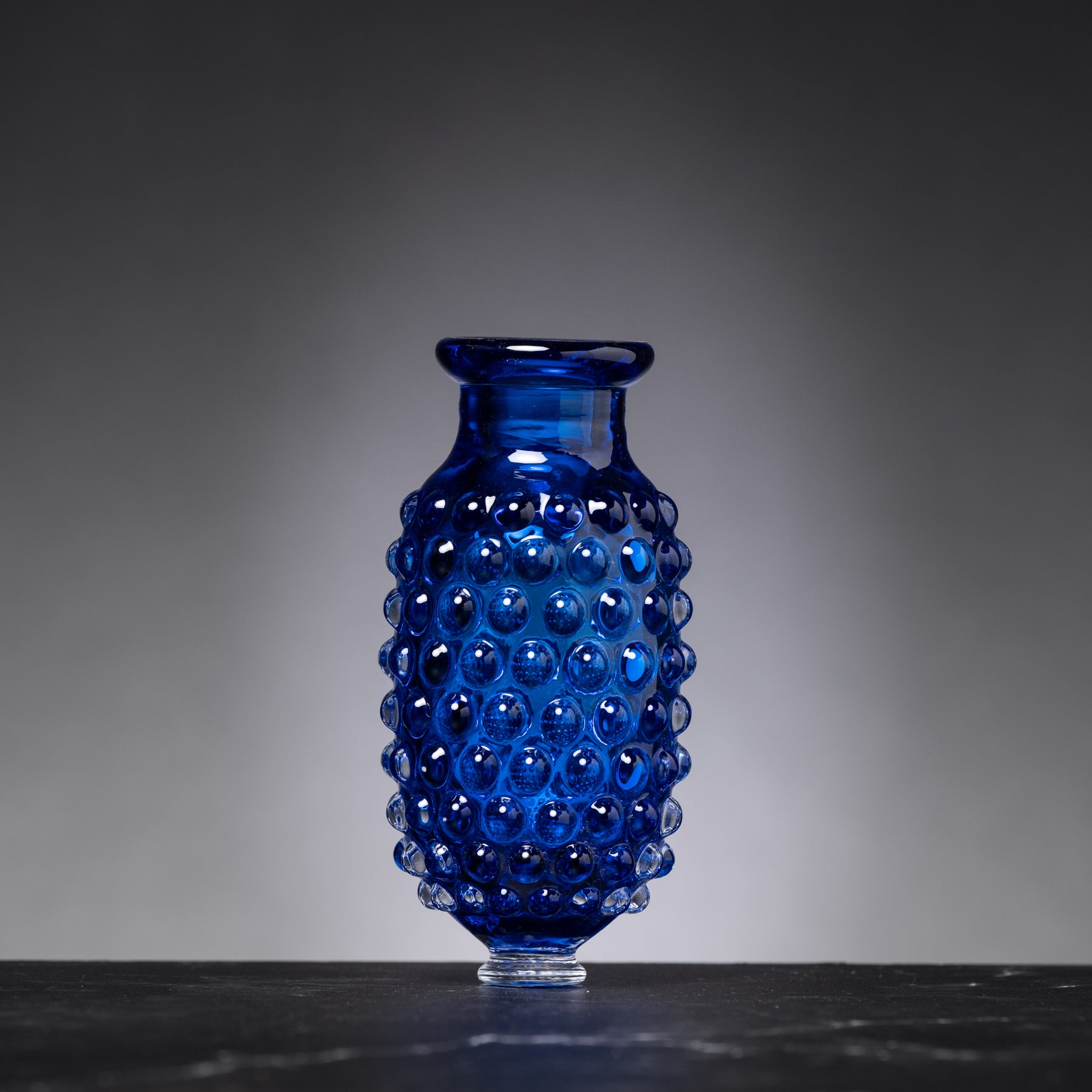 Blue glass vase with a textured surface on a dark surface and gray background