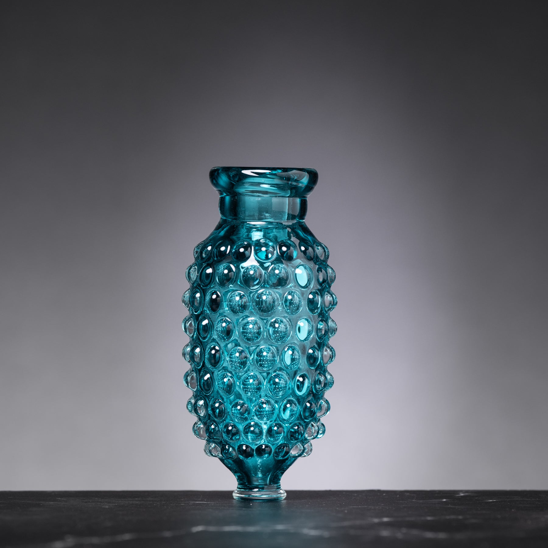 Blue glass vase with a textured surface on a dark surface and gray background