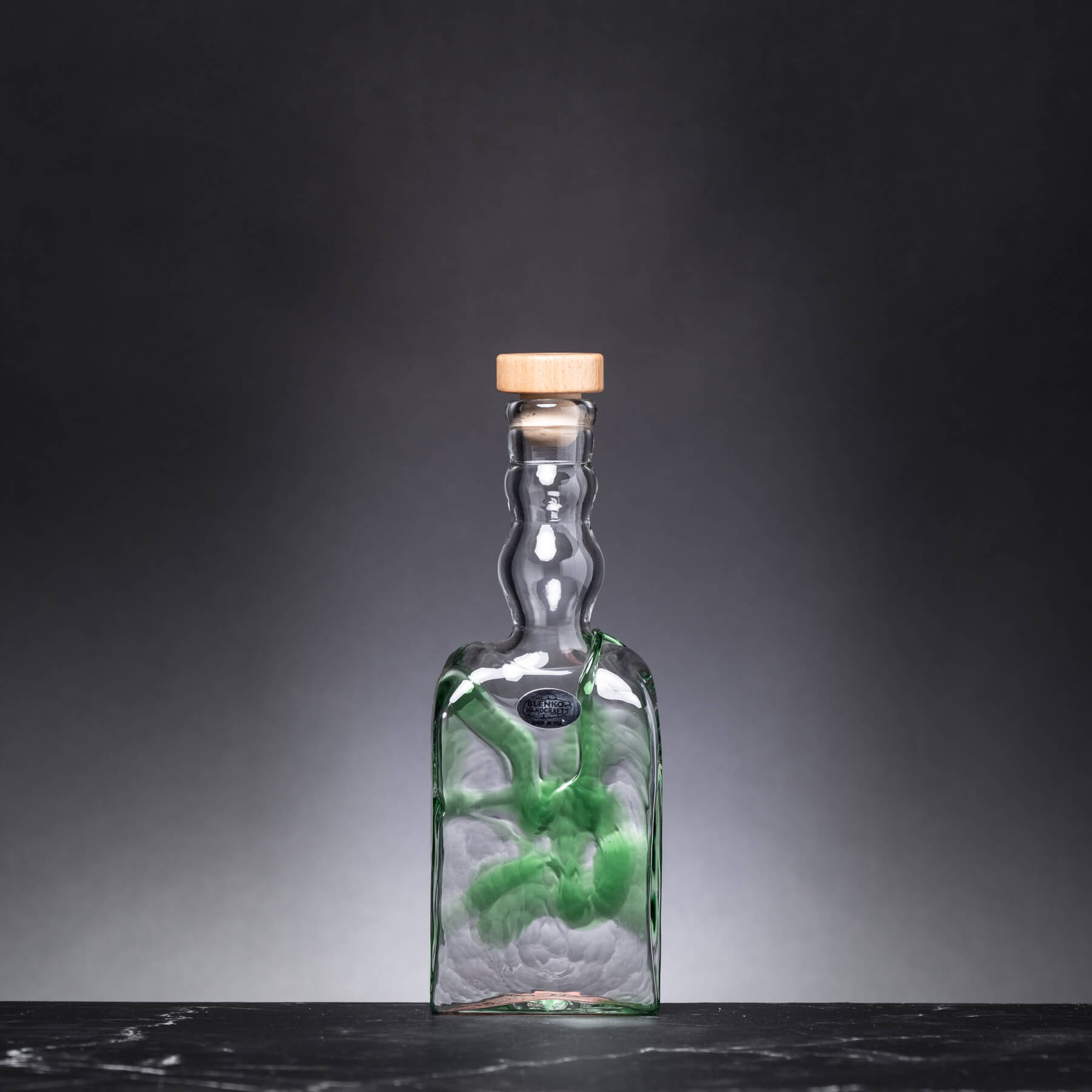 Glass bottle with a cork lid on a dark surface and gray background