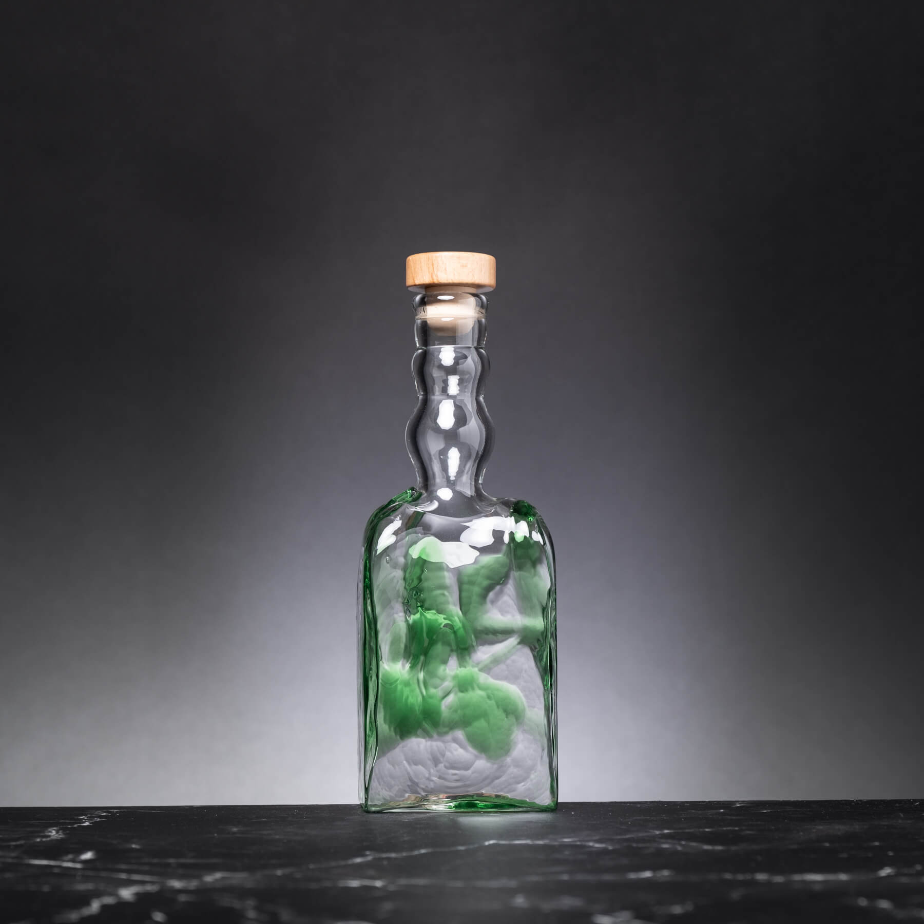 Glass bottle with a cork lid on a dark surface and gray background
