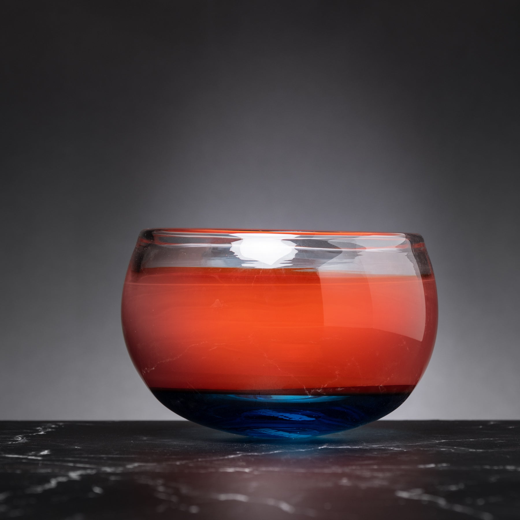 Glass bowl with red and blue gradient on a dark surface and gray background