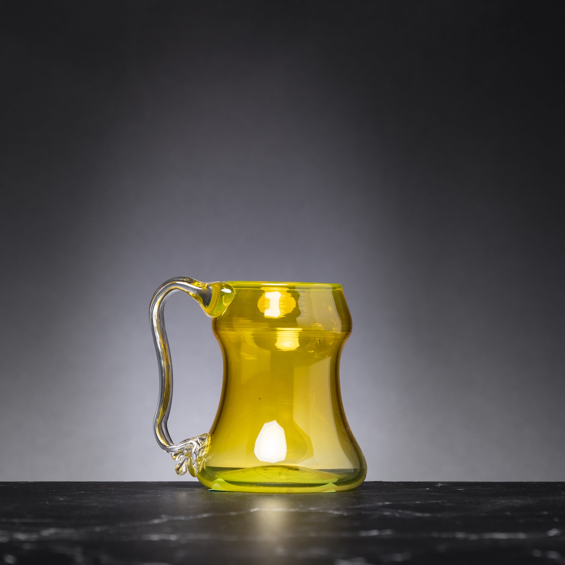 Yellow glass mug on a dark surface with a gray background