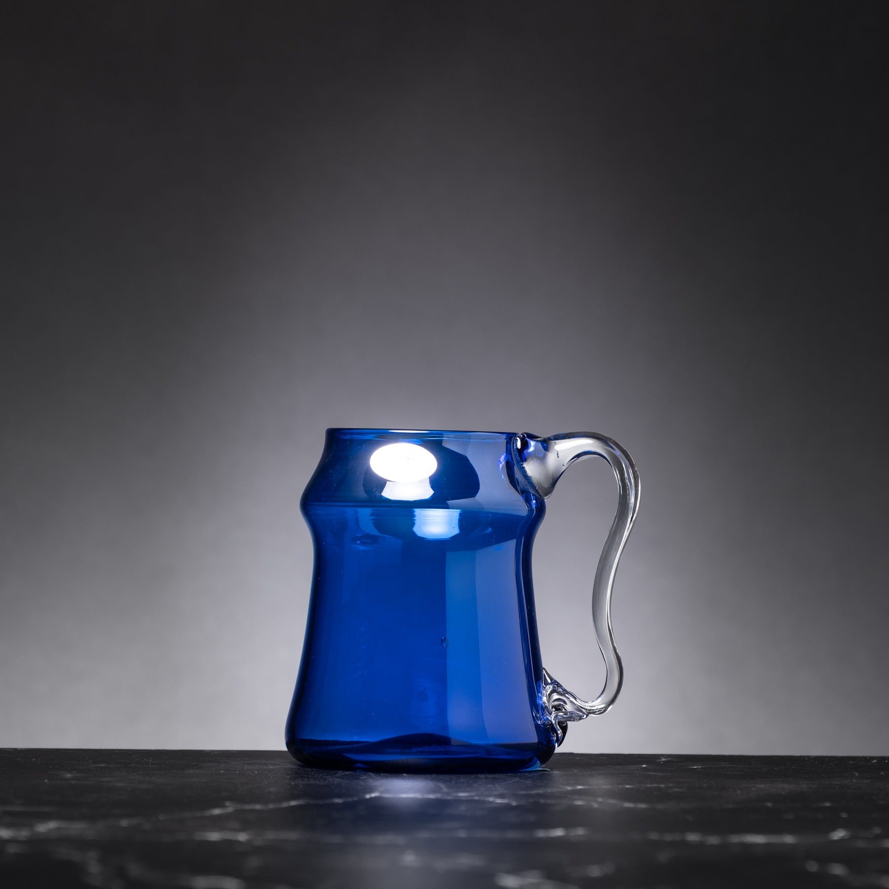 Blue glass mug on a dark surface with a gray background