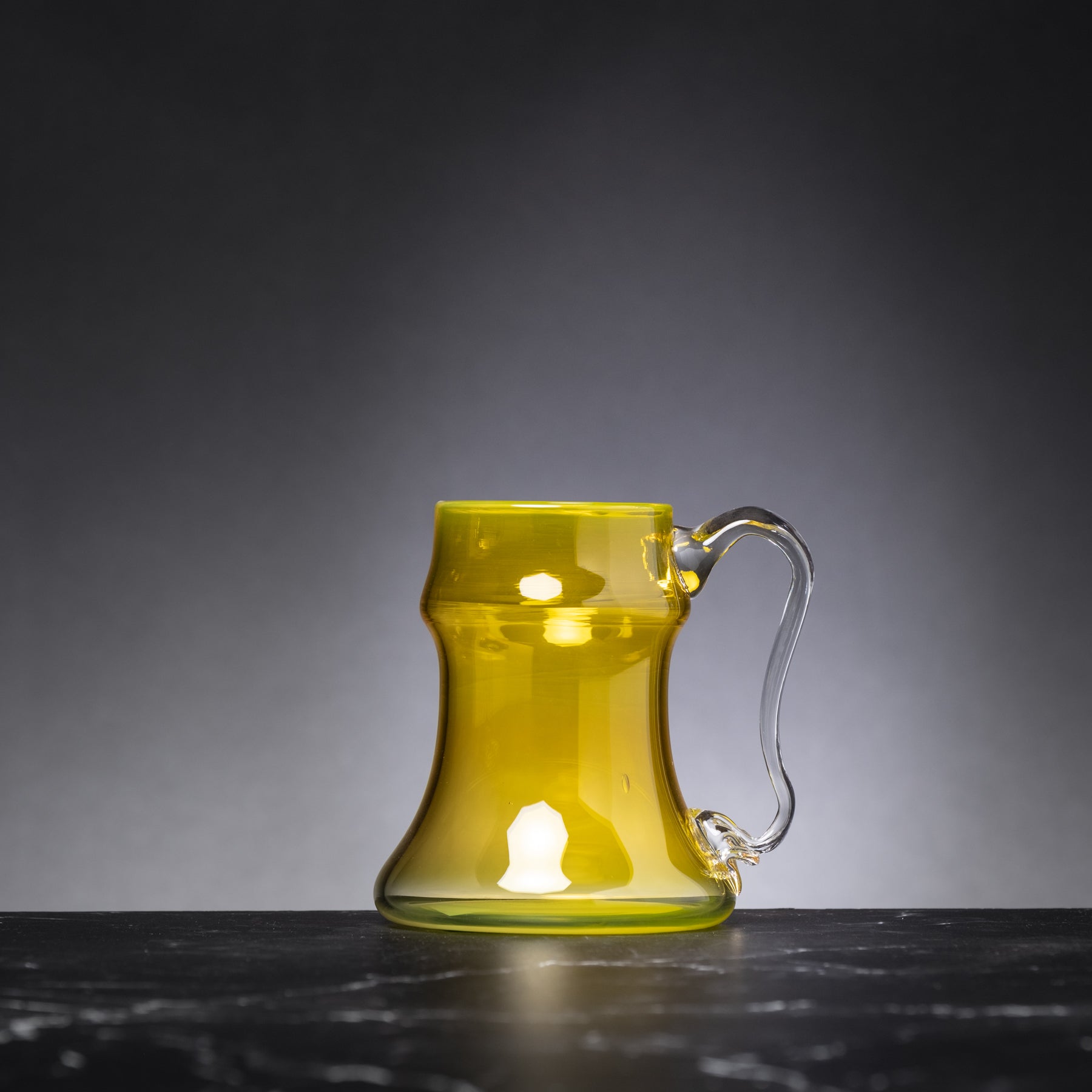 Yellow glass mug with handle on a dark surface and gray background