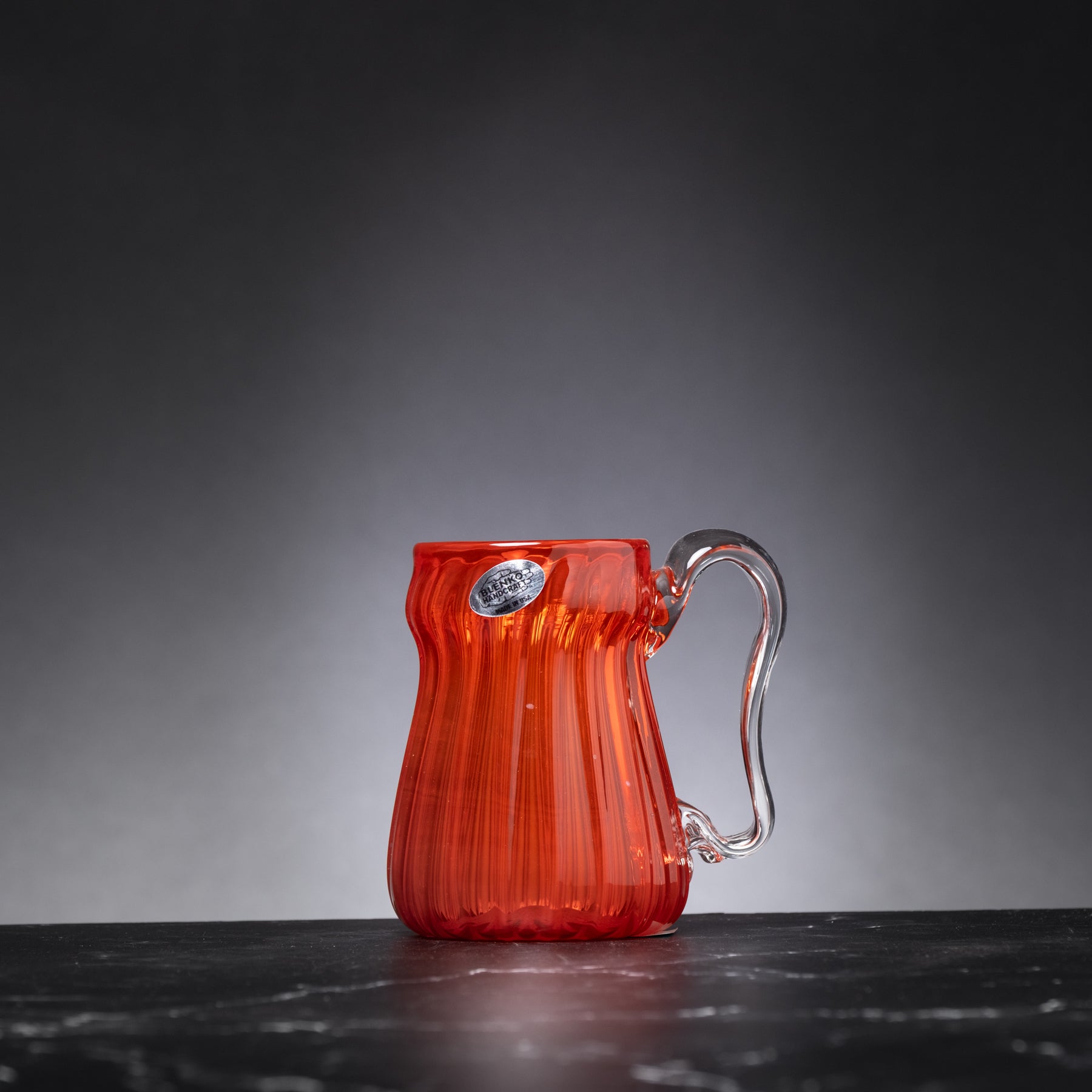 Red glass pitcher with a handle on a dark surface and gray background
