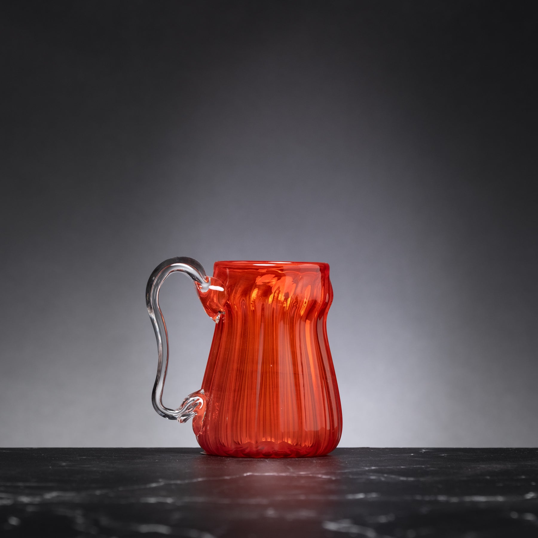 Red glass mug with a handle on a dark surface and gray background