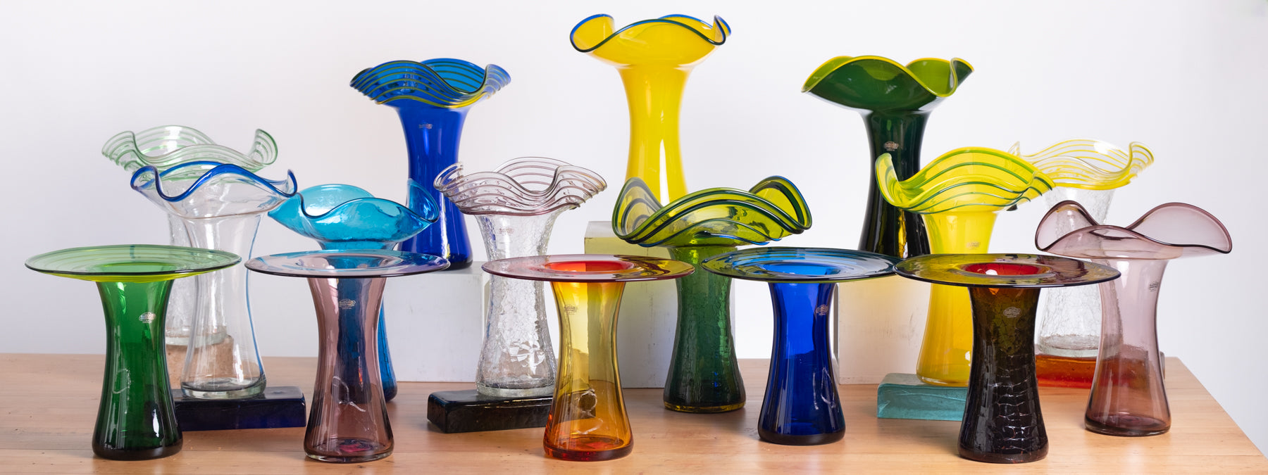 Collection of colorful glass vases on a wooden surface with a white background