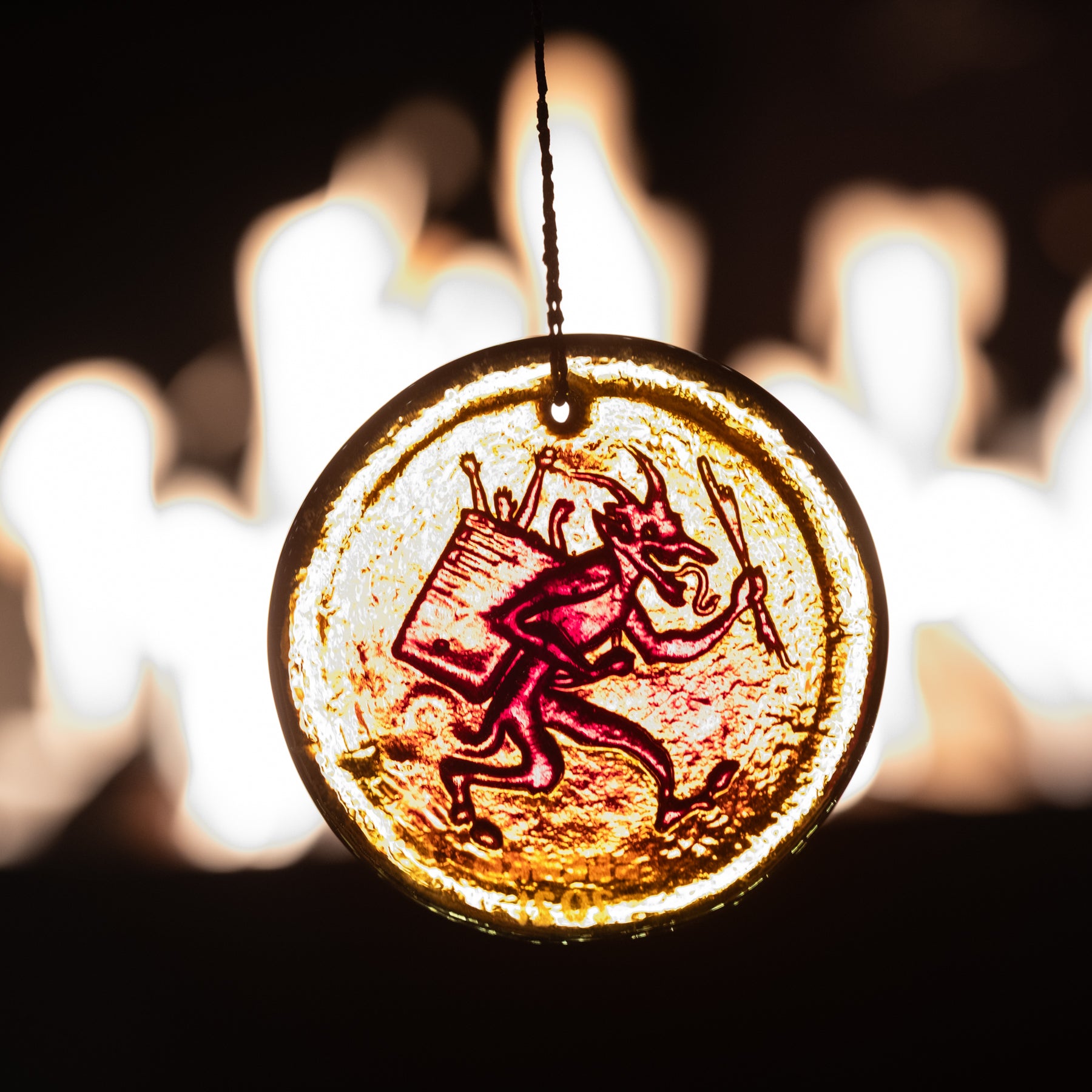 Decorative pendant with a red devil illustration against a blurred candlelight background