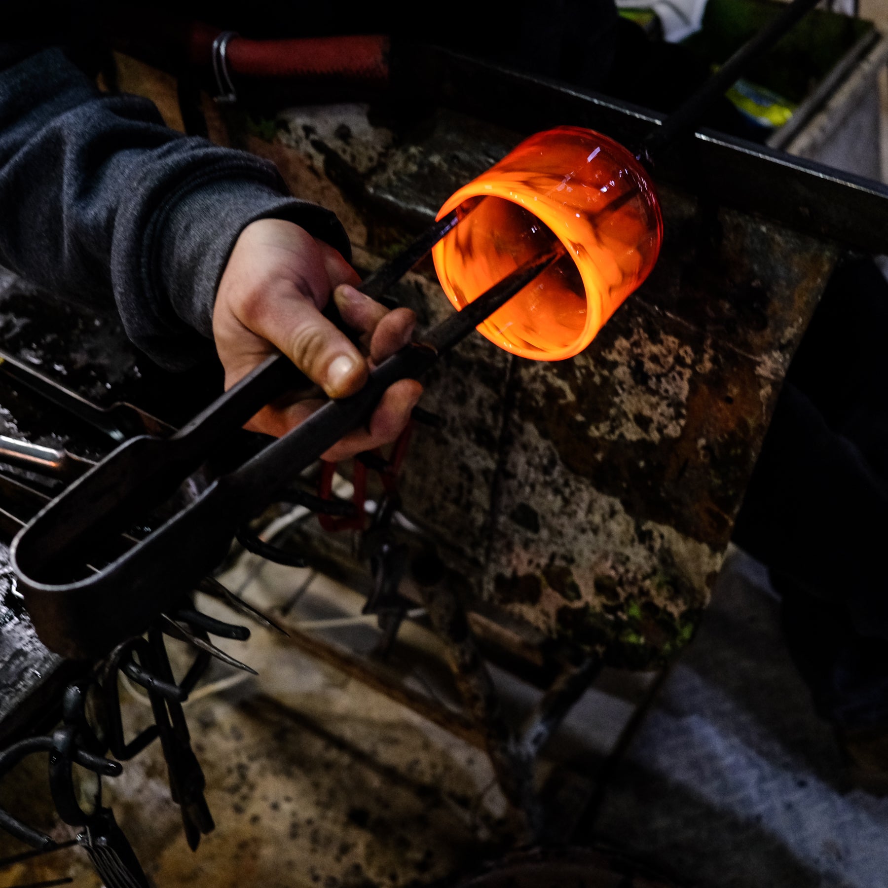 Person holding a glowing red-hot metal object with tongs in a workshop setting