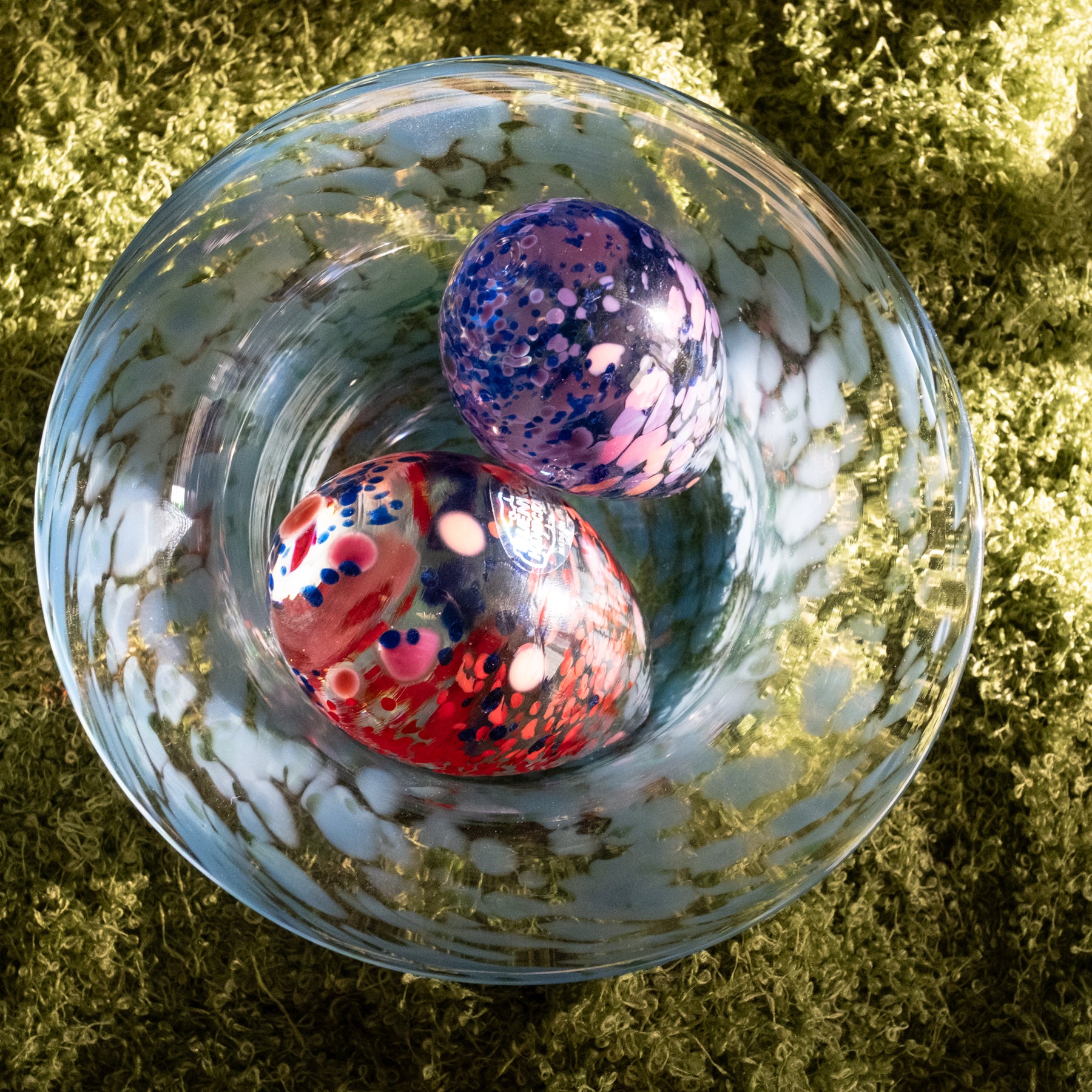 Two colorful marbles in a glass bowl on a grassy background