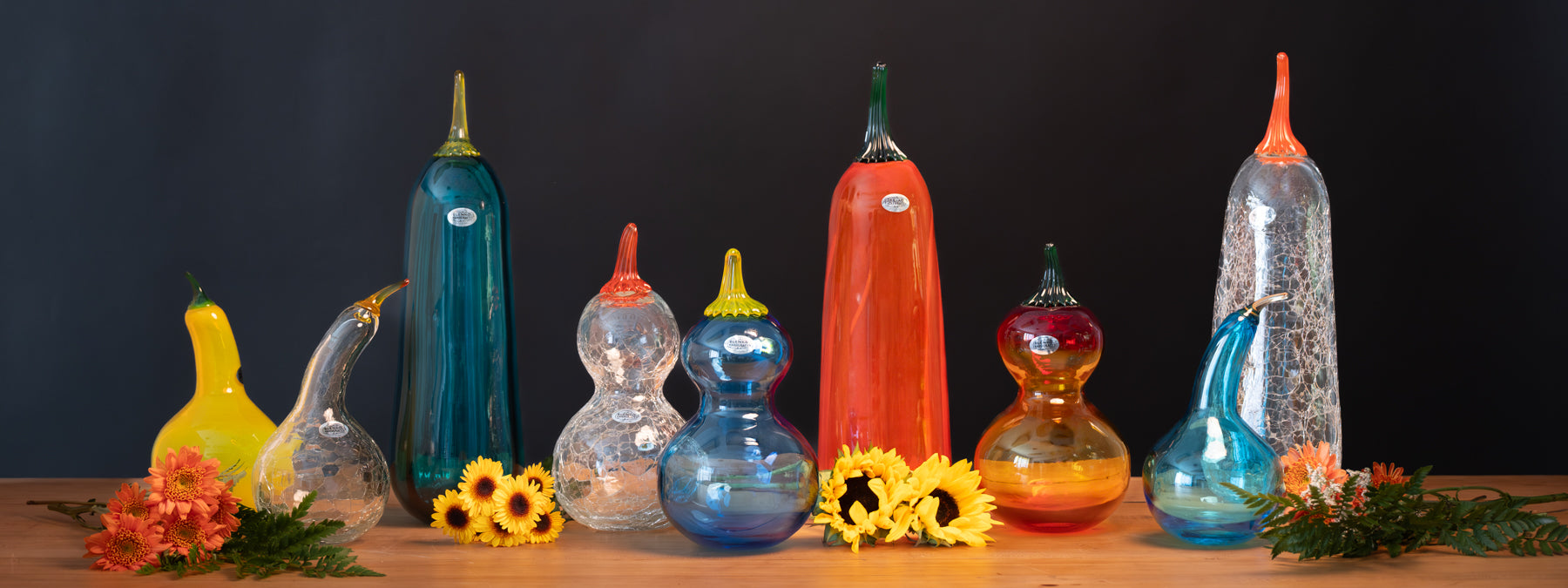 Collection of colorful glass sculptures on a wooden surface with a dark background