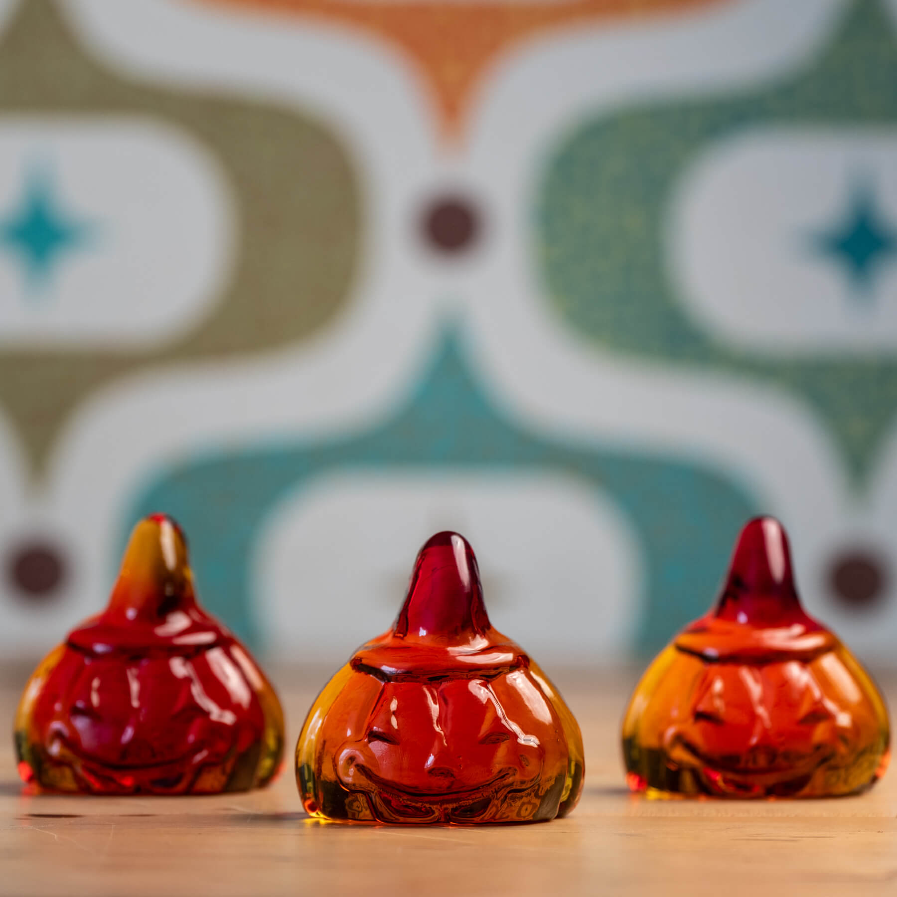 Three pumpkin figurals on a wooden surface with a patterned background