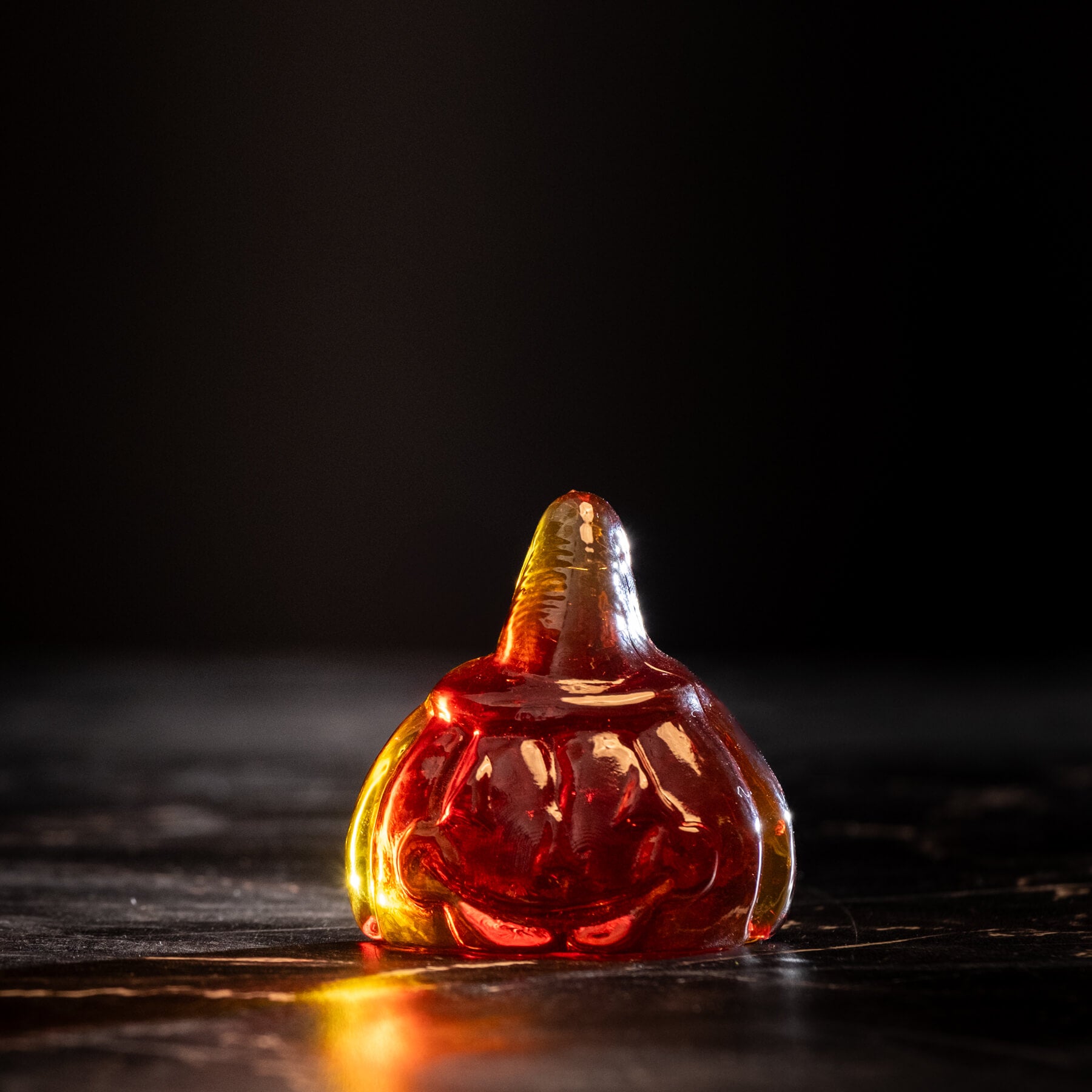 Glass pumpkin figurine with a smiling face on a dark background