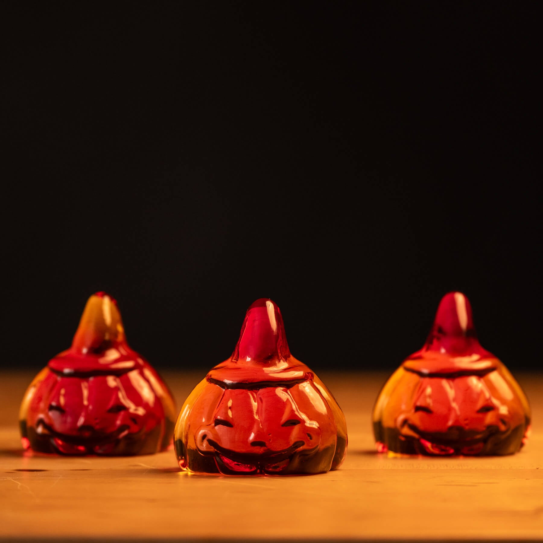 Three glass pumpkins with jack-o'-lantern faces on a wooden surface with a dark background